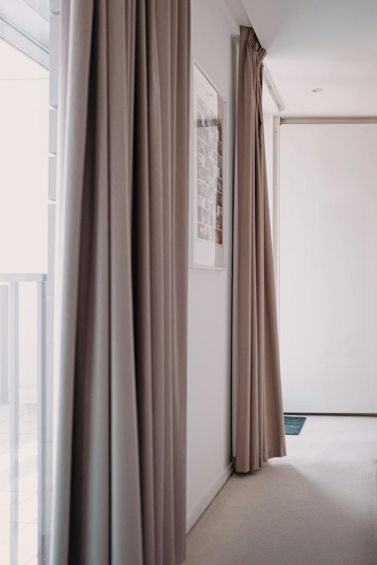 Modern curtain ideas for the living room showcasing long, flowing drapes in an elegant accent in greige. The curtains frame a bright, minimalistic space with white walls and clean lines, adding warmth, softness, and a versatile neutral touch that works beautifully in both contemporary and classic interiors.