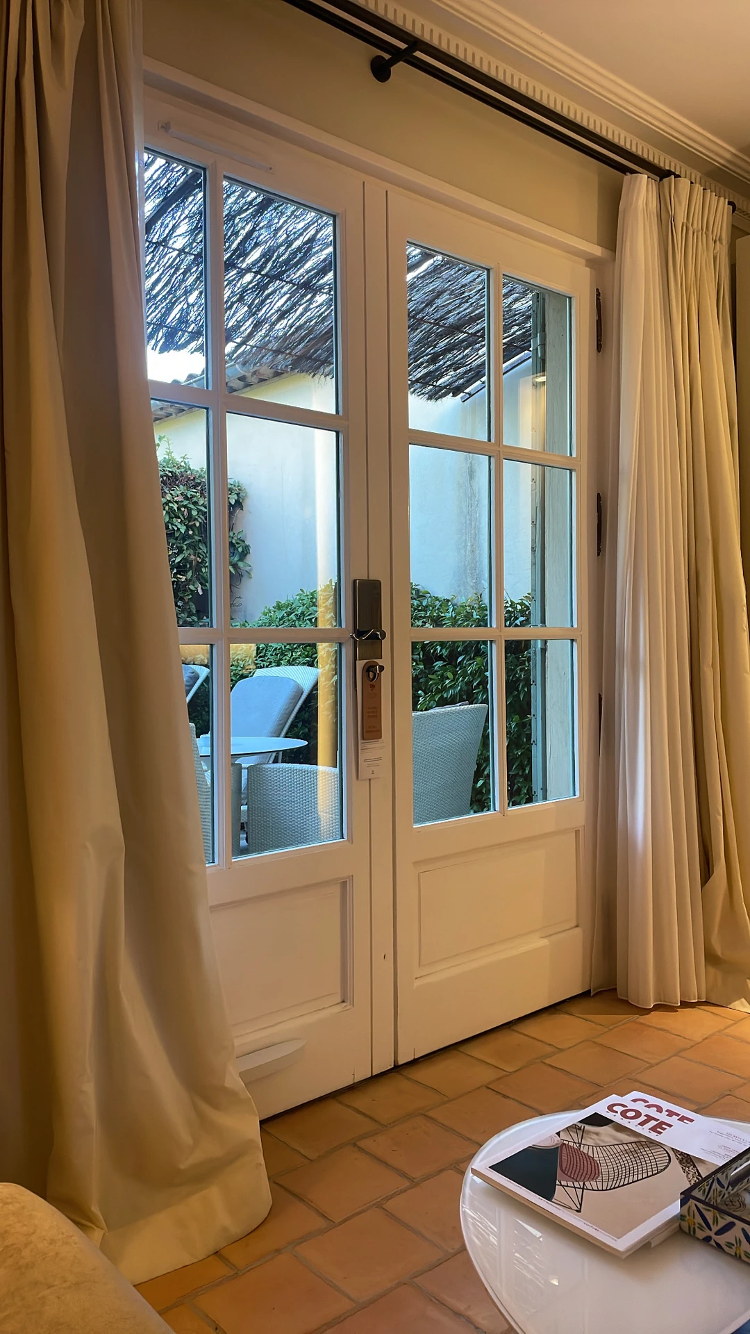 Elegant curtain ideas for the living room featuring heavy valuable curtains in a soft beige tone, framing classic French doors that open to a cozy patio. The thick fabric provides both privacy and a luxurious touch, blending functionality with timeless style in a versatile living space.