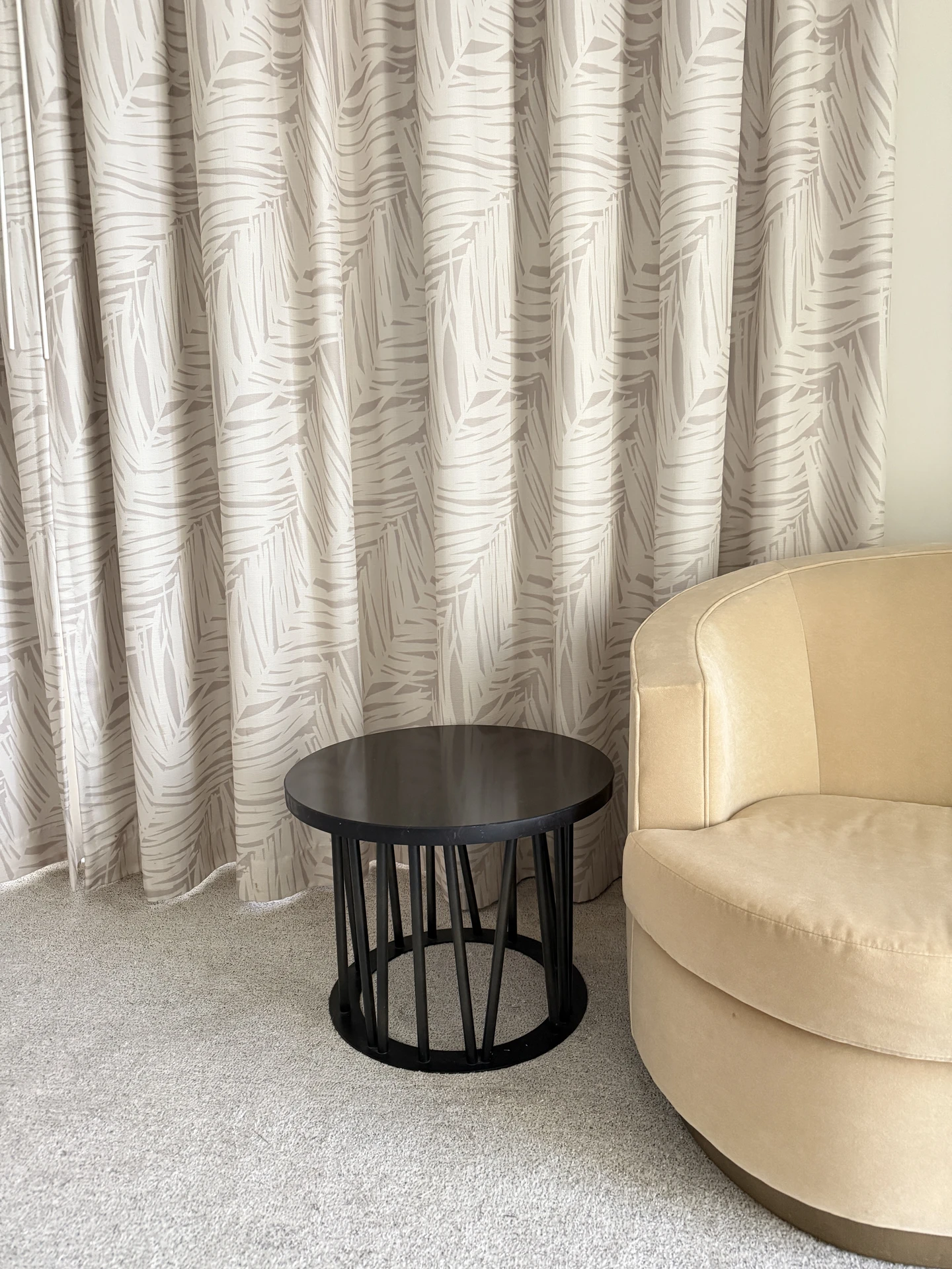 Modern curtain ideas for the living room featuring elegant beige drapes with a subtle leaf pattern, adding texture and depth to the space. The curtains are paired with a round beige armchair and a sleek black side table, creating a versatile and cozy corner that balances natural inspiration with contemporary style.