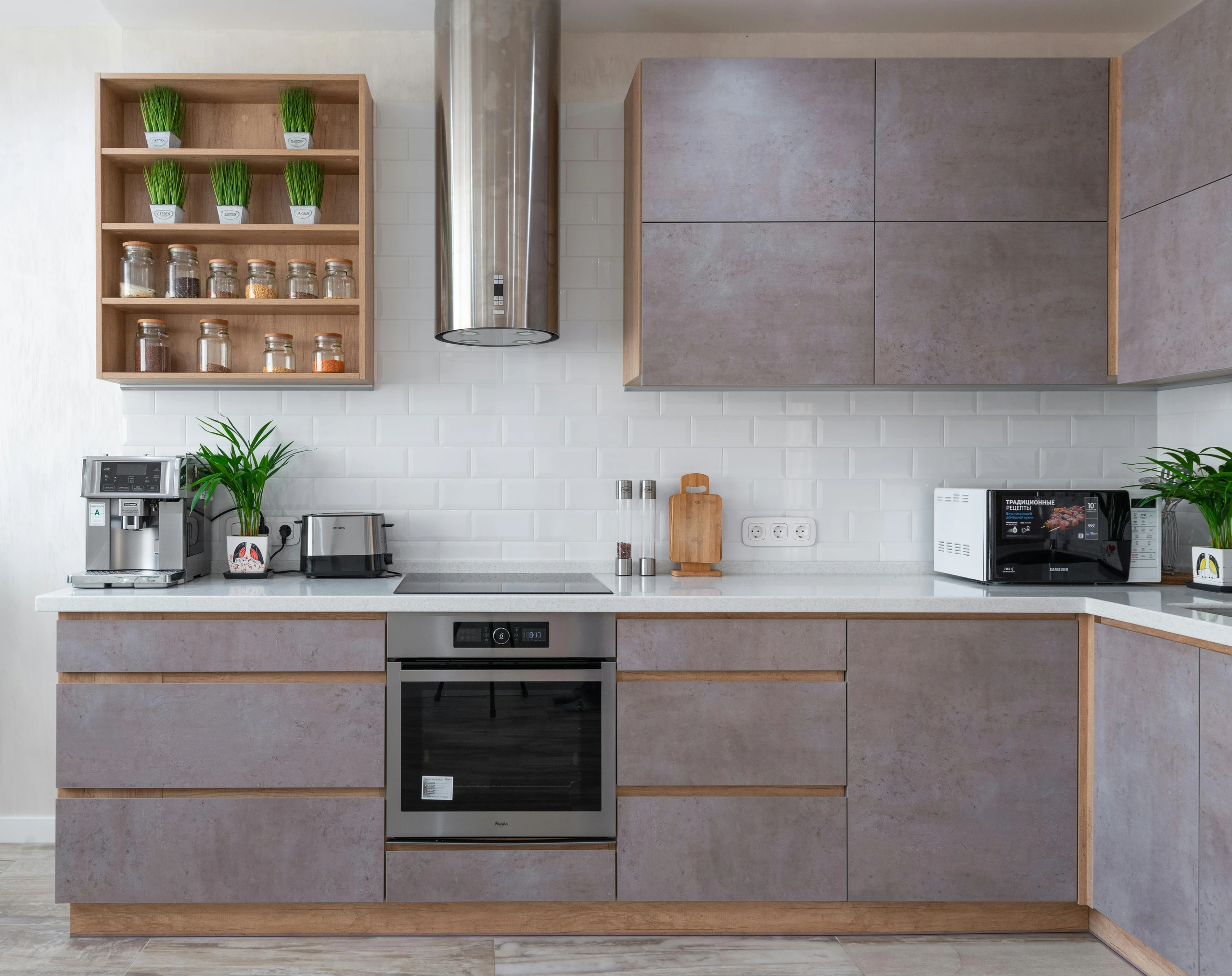 Modern kitchen showcasing smart kitchen counter organization with a “create sections on your kitchen counter” approach. On the left, a coffee station features an espresso machine, toaster, and potted plant, while the right side serves as a cooking prep area with a microwave, cutting board, spice mills, and another plant. Open shelving above stores small jars of dry goods and decorative greenery, keeping everything neatly separated and visually balanced.