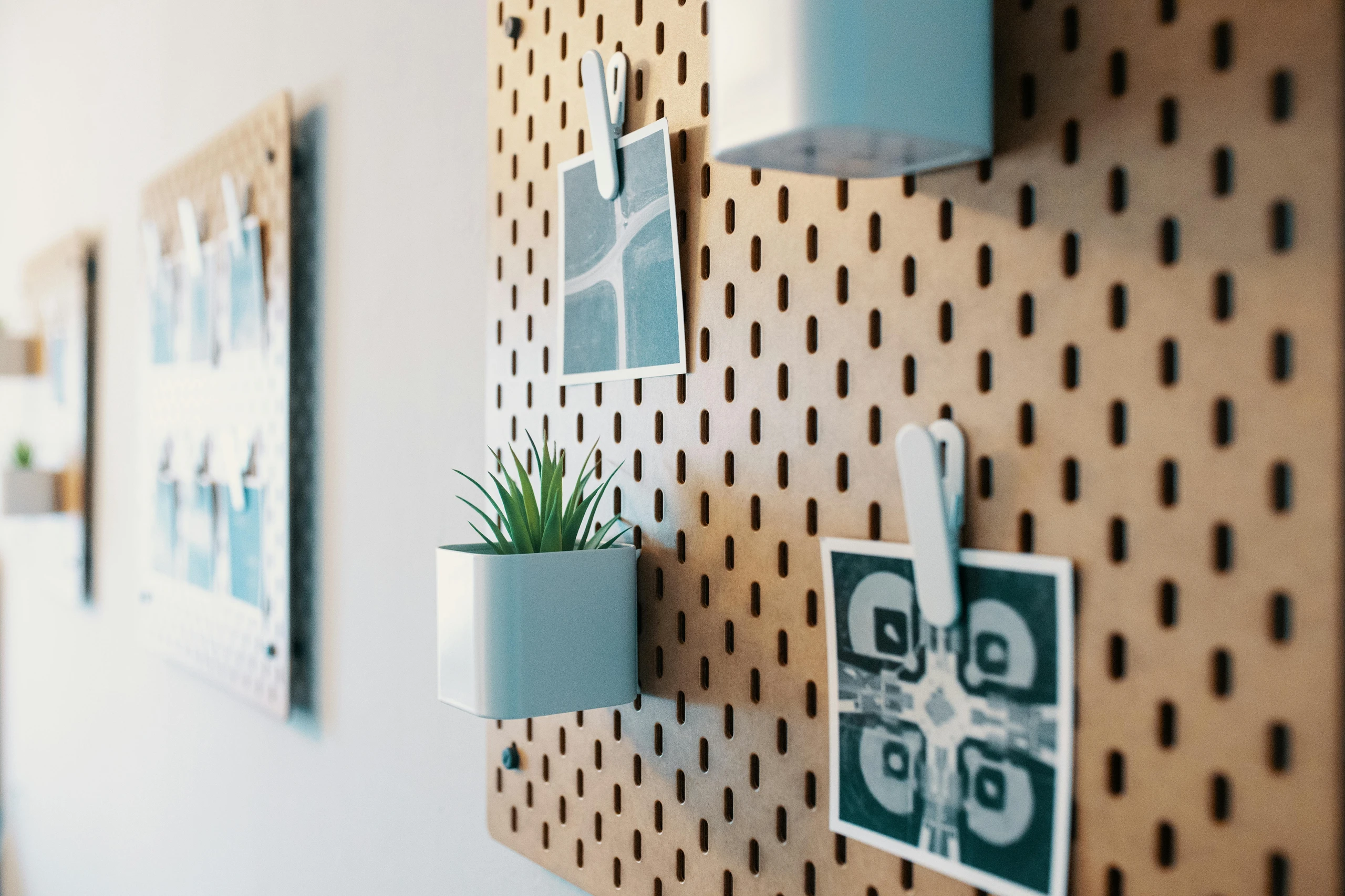 Creative kitchen counter organization idea featuring a pegboard mounted on the wall, used to hold small planters, photos, and notes with clips. The light brown pegboard has a modern, versatile look, offering endless possibilities for storing utensils, hanging baskets, or displaying decorative pieces to keep the counter clutter-free while adding personality to the kitchen.