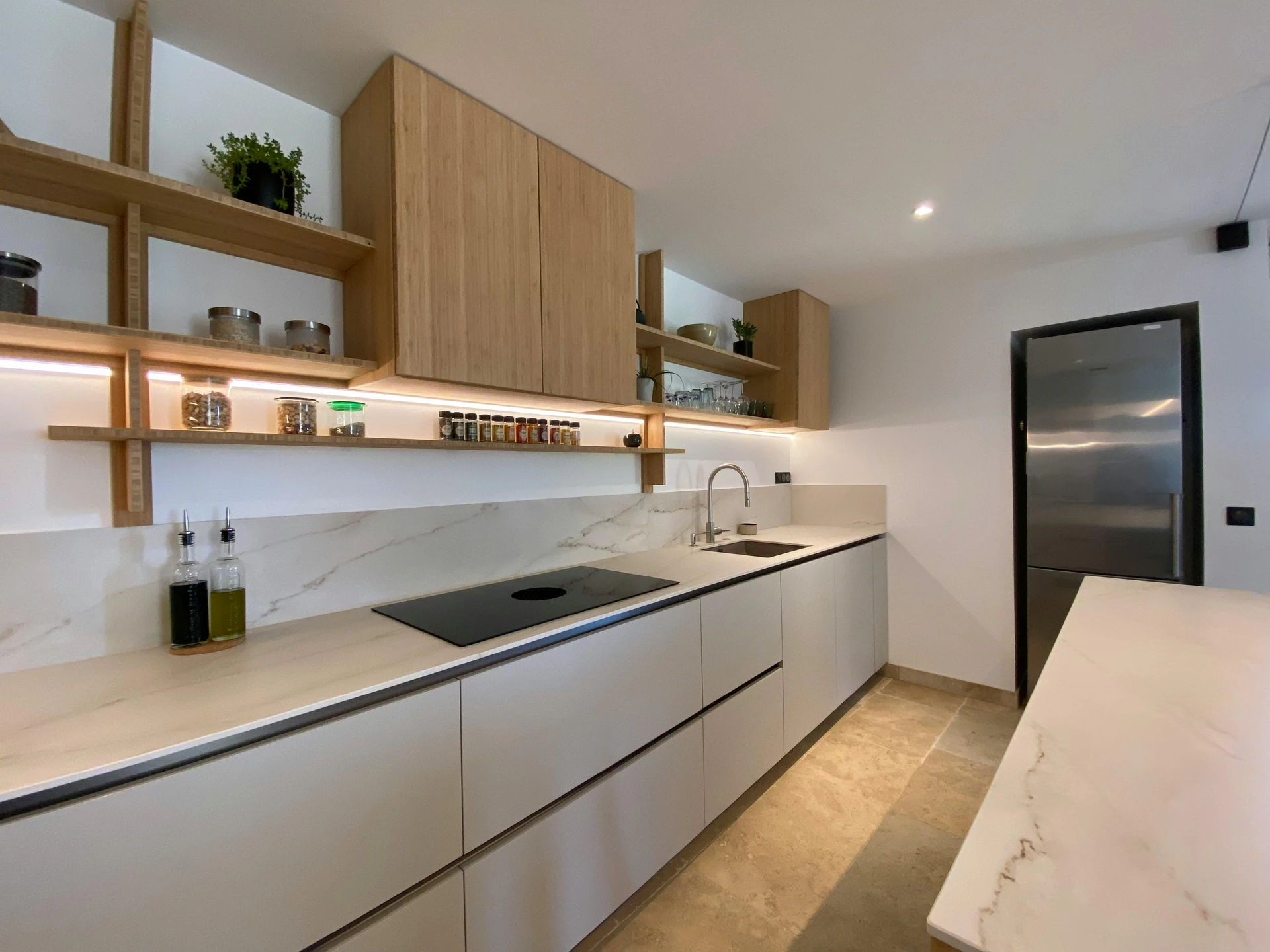 A modern kitchen with light wood cabinetry and marble countertops, featuring neatly arranged open shelves displaying jars of spices, dry goods, glassware, and small potted plants. The thoughtful placement shows how to organize open shelves for both style and function, making it an inspiring example of kitchen organization ideas for small kitchens where every inch of space is maximized.