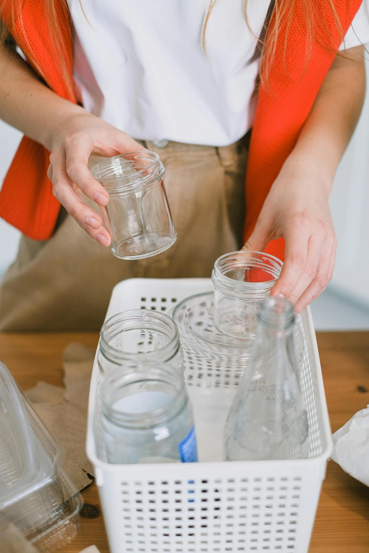 A person organizing empty glass jars and bottles in a white perforated plastic container, demonstrating how to use plastic boxes for storage as part of practical kitchen organization ideas for small kitchens. The setup shows a versatile approach to keeping reusable containers neatly arranged and easy to access.