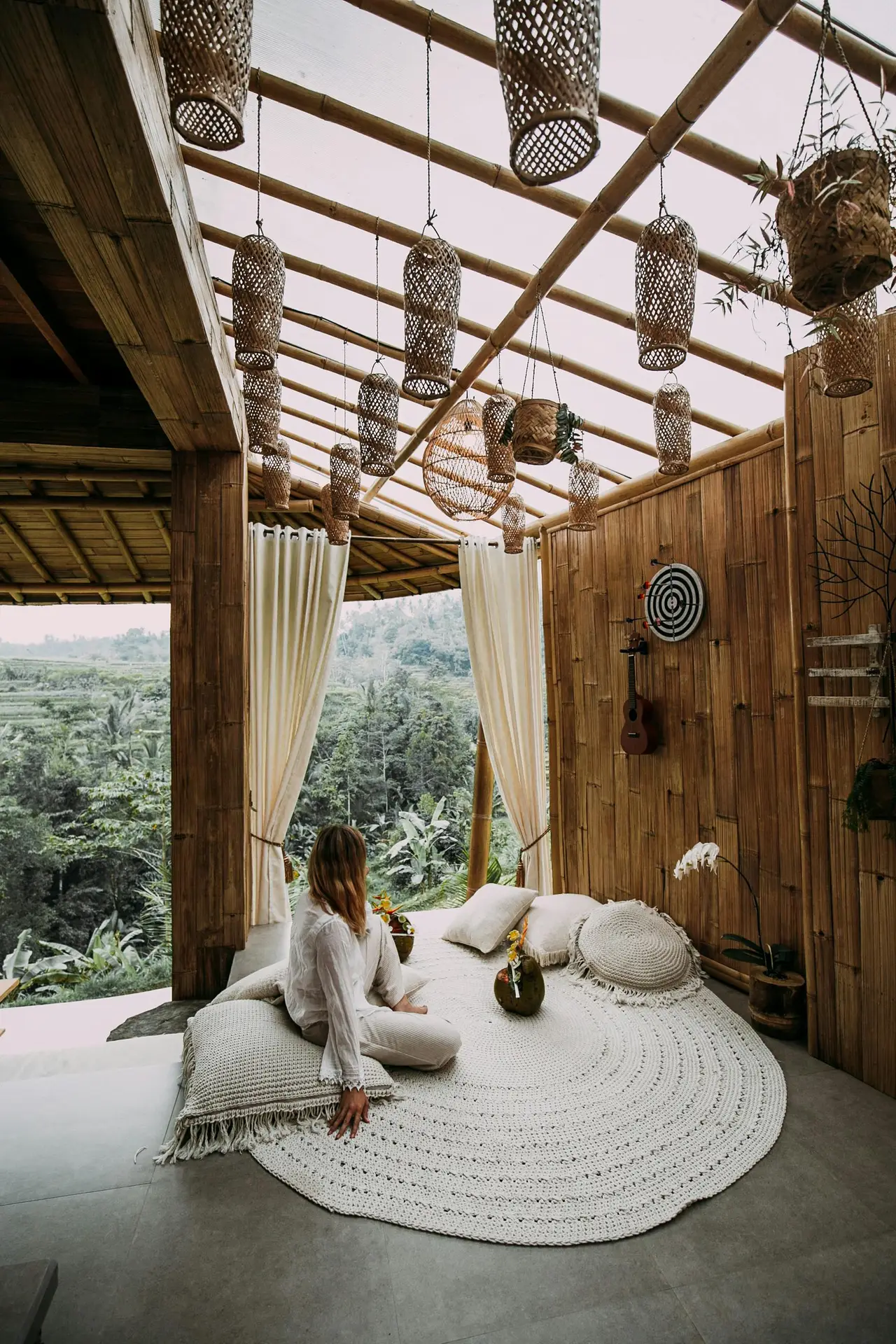 A serene bamboo-style balcony with flowing curtains, woven hanging lanterns, and a cozy carpeted seating area filled with cushions and throws, overlooking lush greenery. Perfect for those looking for natural and bohemian balcony decoration ideas that invite relaxation and connection with nature.