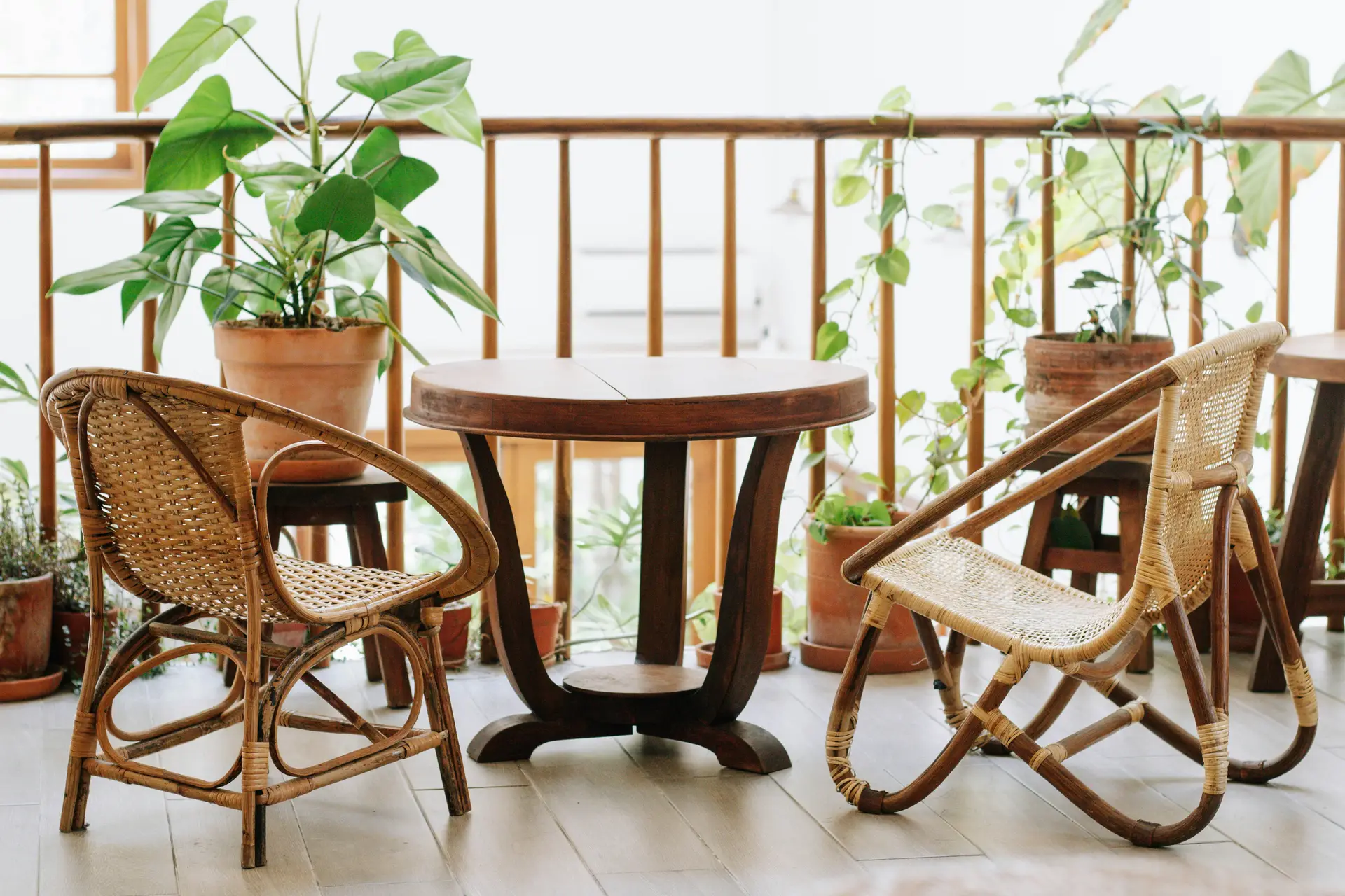 Cozy setup with rattan balcony chairs and a round wooden table surrounded by lush potted plants, offering natural charm and inspiring balcony decoration ideas. The mix of earthy textures, greenery, and simple wooden railing creates a calm retreat perfect for coffee, reading, or relaxing outdoors.