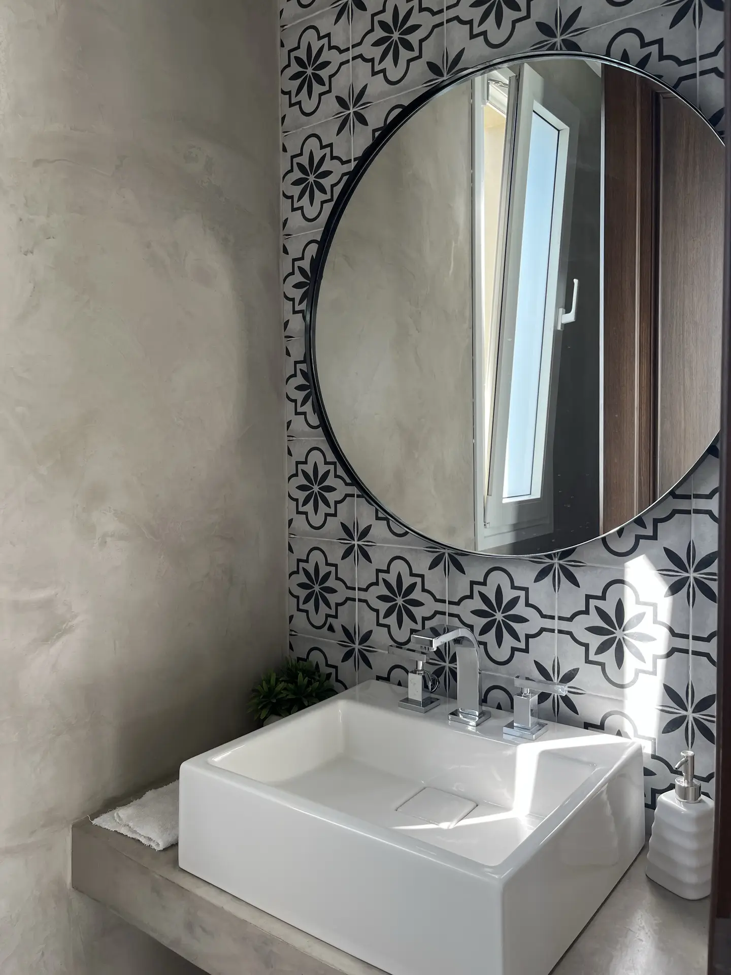 Modern vanity with a square white basin and chrome faucet, set against a striking accent wall of black-and-white encaustic tiles, offering bold pattern inspiration for bathroom tiles ideas that combine contemporary style with timeless character.