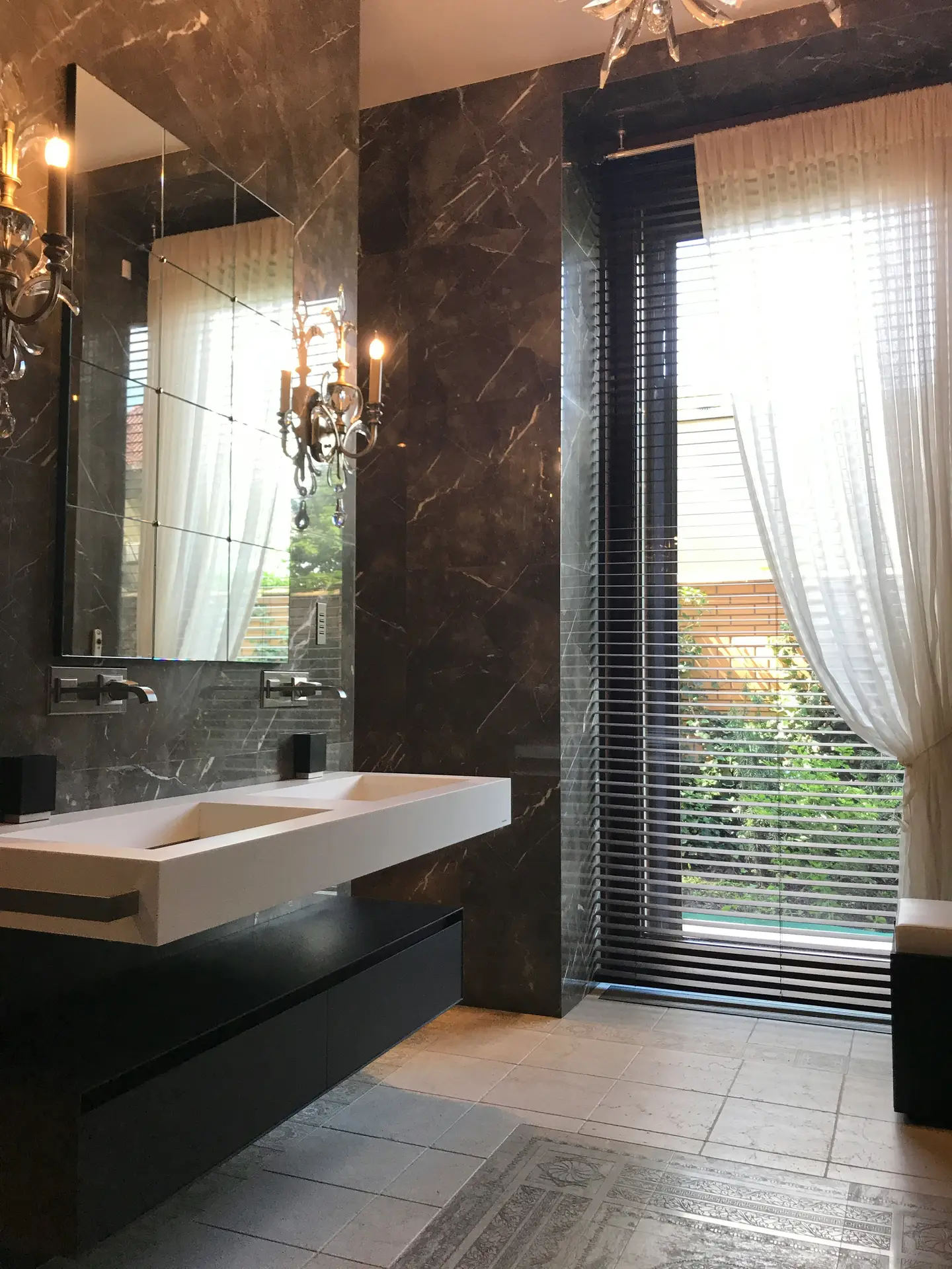 Luxurious bathroom showcasing glossy dark marble tiles with subtle veining, a floating double sink vanity, and wall-mounted faucets, paired with tall windows and sheer curtains, providing refined bathroom tiles ideas for an elegant and dramatic design.