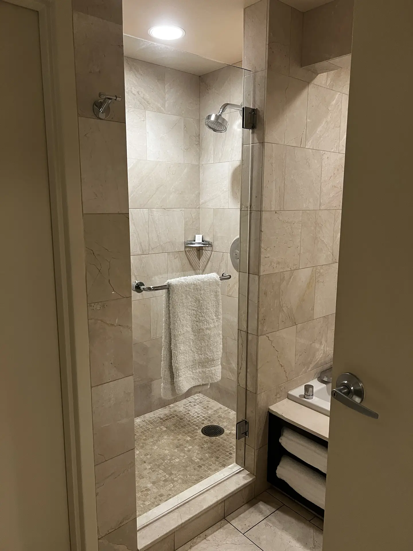Walk-in shower featuring large beige marble-effect tiles with mosaic shower floor, accented by a glass door and chrome fixtures, offering practical yet stylish inspiration for modern bathroom tiles ideas that balance elegance and durability.