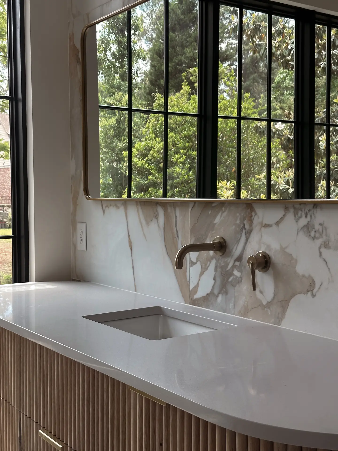 Elegant bathroom vanity with a sleek white countertop, brass fixtures, and a large mirror framed in gold, set against stunning marble wall tiles that bring timeless luxury. An inspiring showcase for modern bathroom tiles ideas blending natural textures with refined finishes.