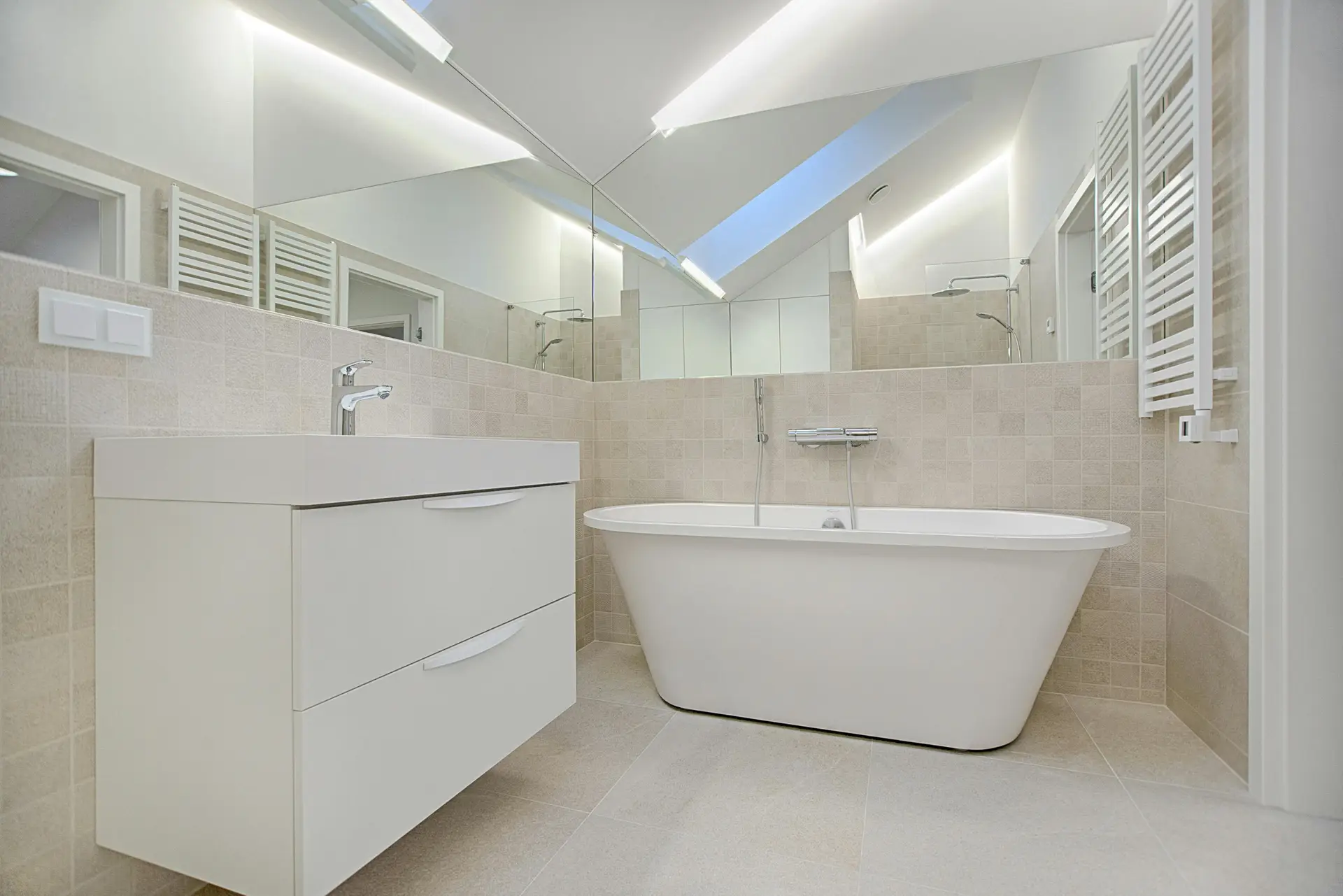 Contemporary bathroom featuring matte beige mosaic tiles on the walls, a sleek floating vanity, and a freestanding bathtub, complemented by large mirrors and hidden lighting, showcasing modern bathroom tiles ideas with a warm and minimal aesthetic.