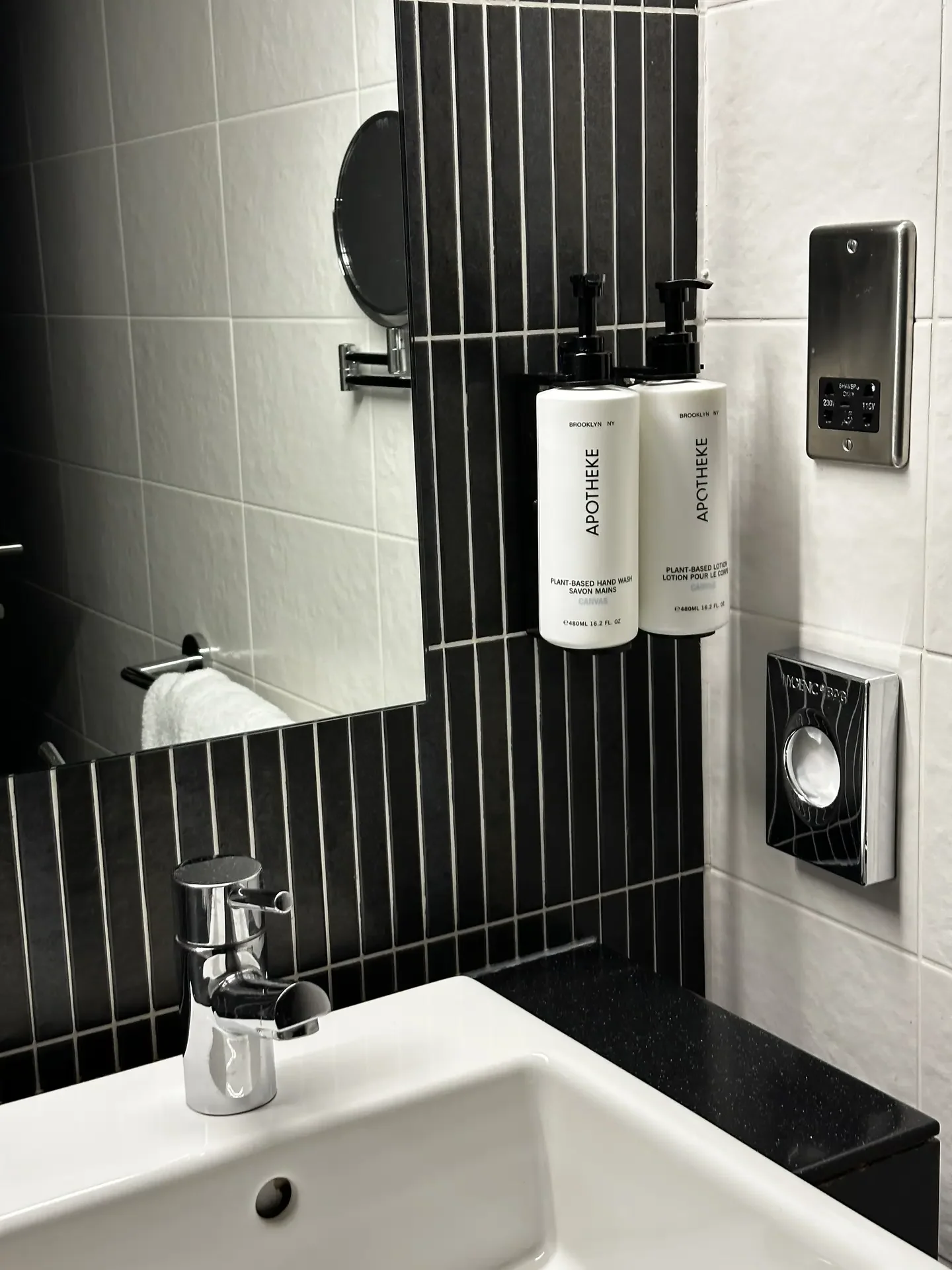 Modern bathroom vanity with a white sink and chrome faucet set against a backdrop of matte black vertical strip tiles, contrasted by white wall tiles above, presenting sleek and contemporary bathroom tiles ideas that highlight bold accents in a minimalist space.