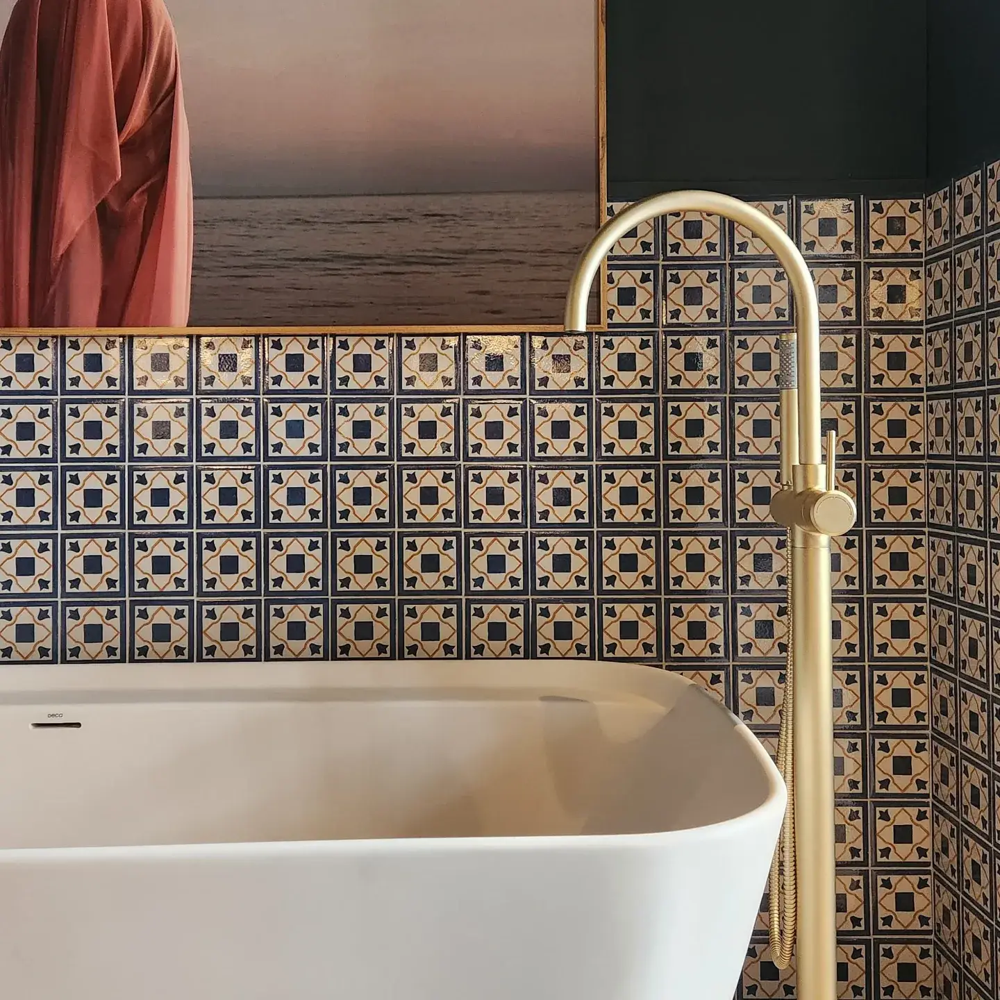 Freestanding bathtub paired with a sleek golden faucet, framed by bathroom tiles ideas featuring bold Mediterranean-style tiles in blue and beige geometric patterns, adding a vibrant and artistic touch to the space.