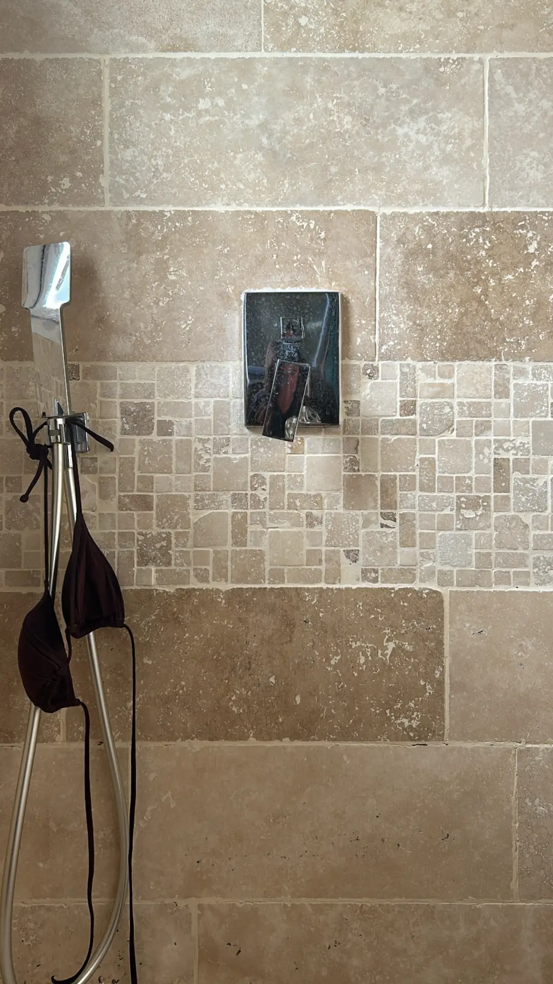 Shower wall finished with tumbled travertine tiles with mixed mosaic accent strip, paired with a chrome control lever and handheld shower, showcasing bathroom tiles ideas that balance rustic textures with a refined modern touch.