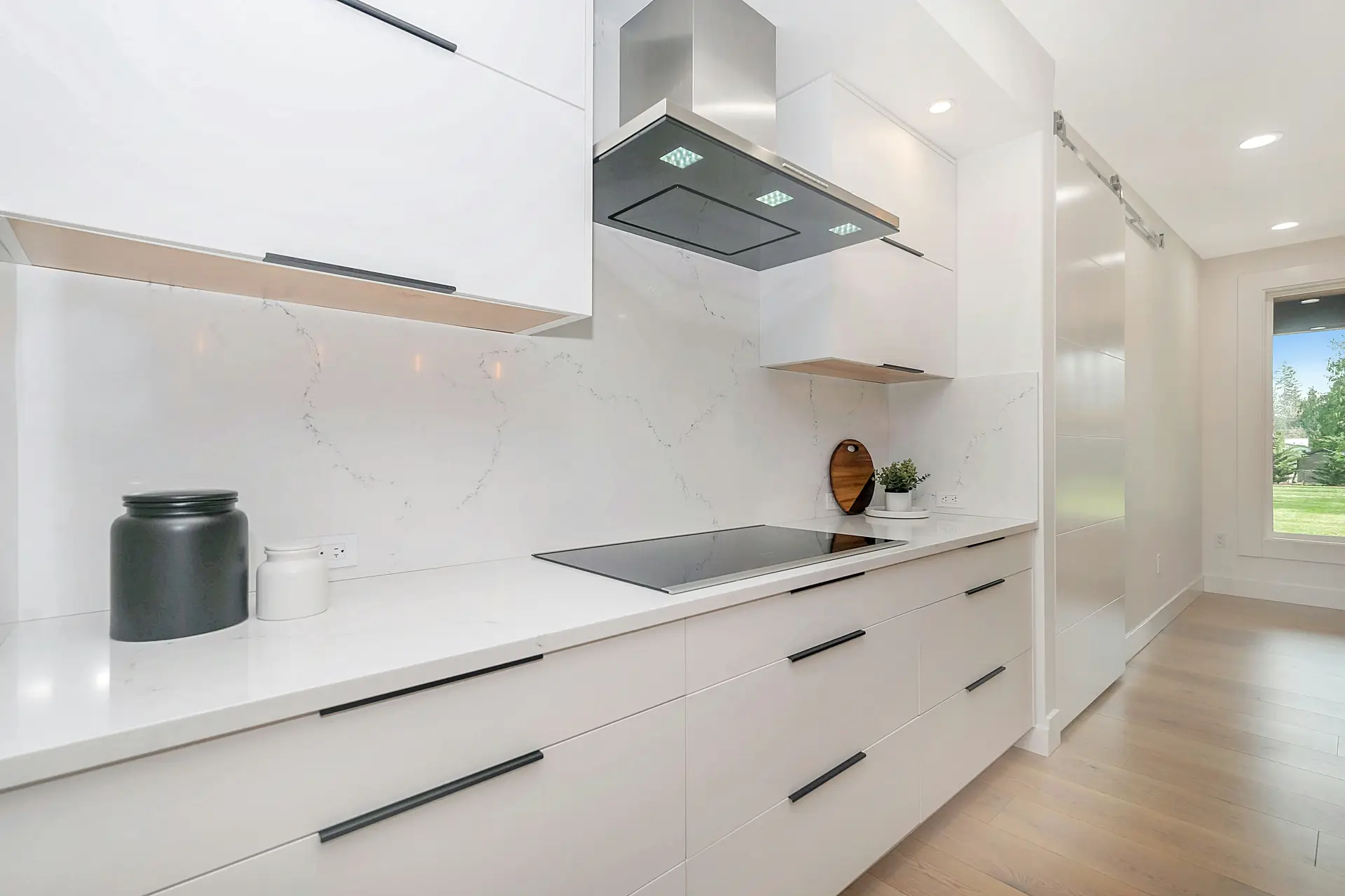 Sleek modern kitchen with glossy white cabinets, black handles, and a smooth induction cooktop. The stainless steel range hood features bright lights under the cooker hood, enhancing both style and function, and offering smart kitchen lighting ideas for effective task illumination in minimalist spaces.