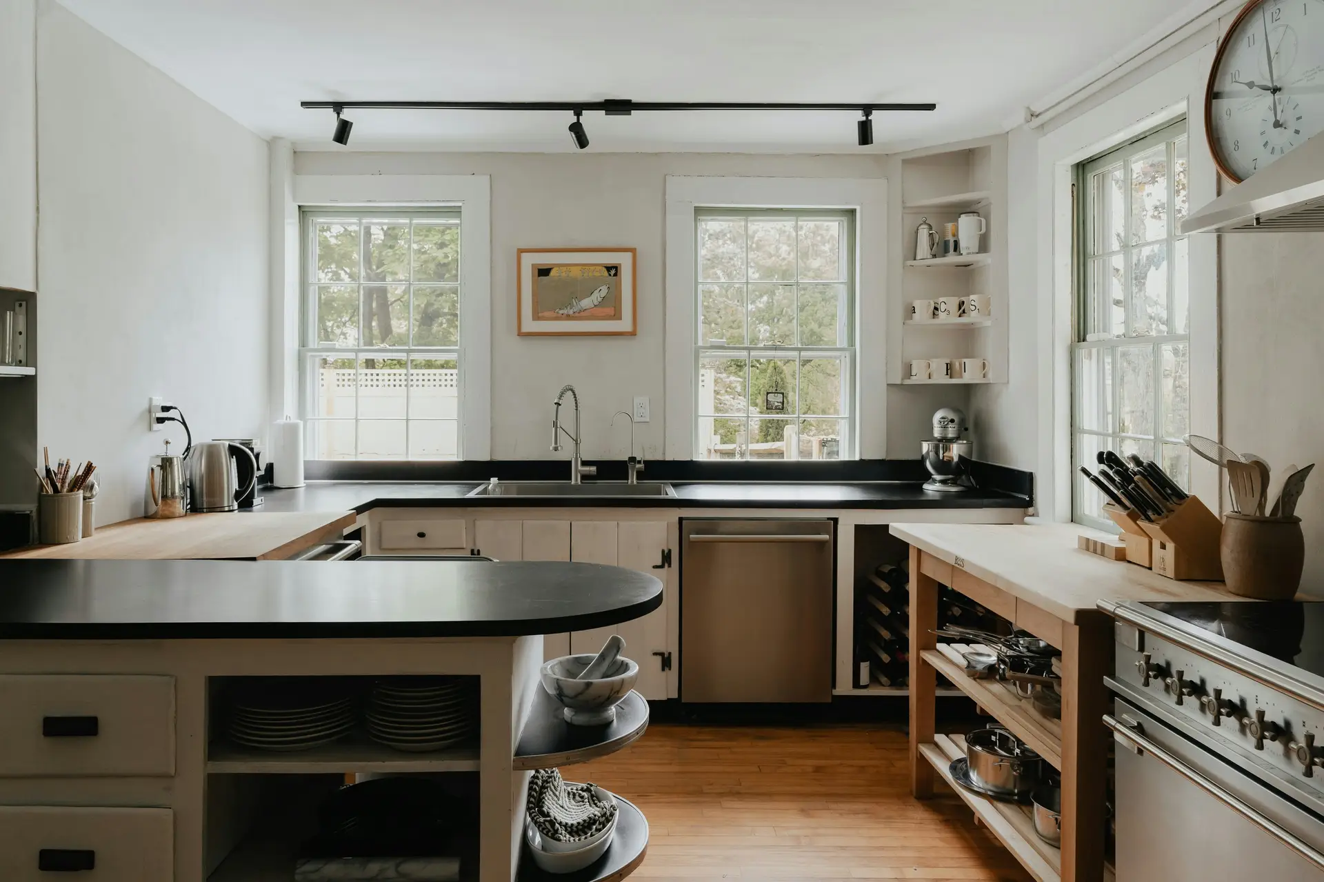 Cozy kitchen with black countertops, open shelving, and a mix of wood and stainless steel accents. A sleek track lighting system runs across the ceiling, providing adjustable illumination and demonstrating versatile kitchen lighting ideas that balance functionality with a modern yet homely aesthetic.