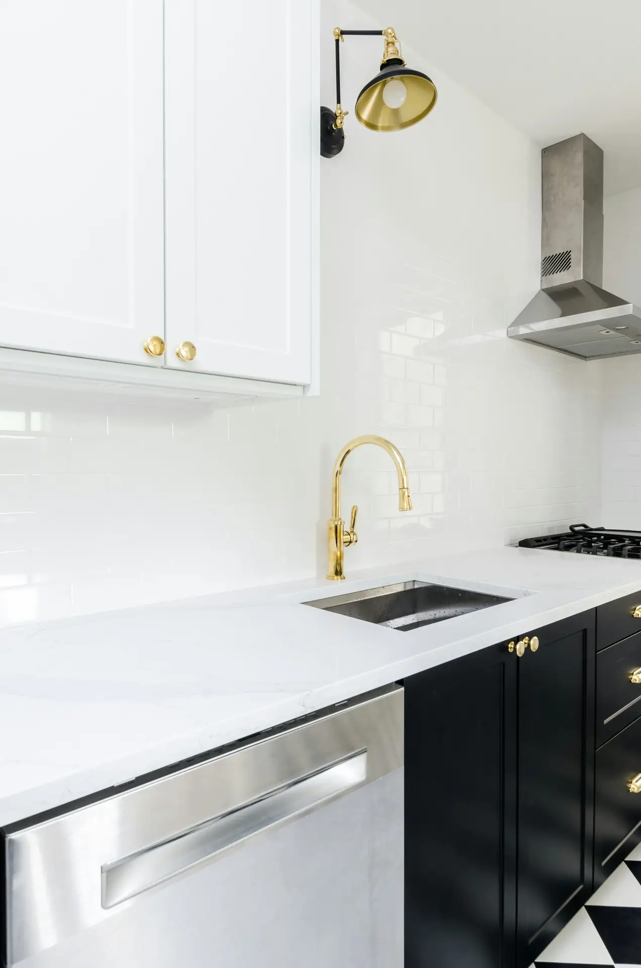 Sleek kitchen with black lower cabinets, white upper cabinets, and brass hardware paired with a matching gold faucet. Above the counter, a stylish wall sconce adds a touch of elegance and function, illustrating kitchen lighting ideas that mix task lighting with modern decorative accents.