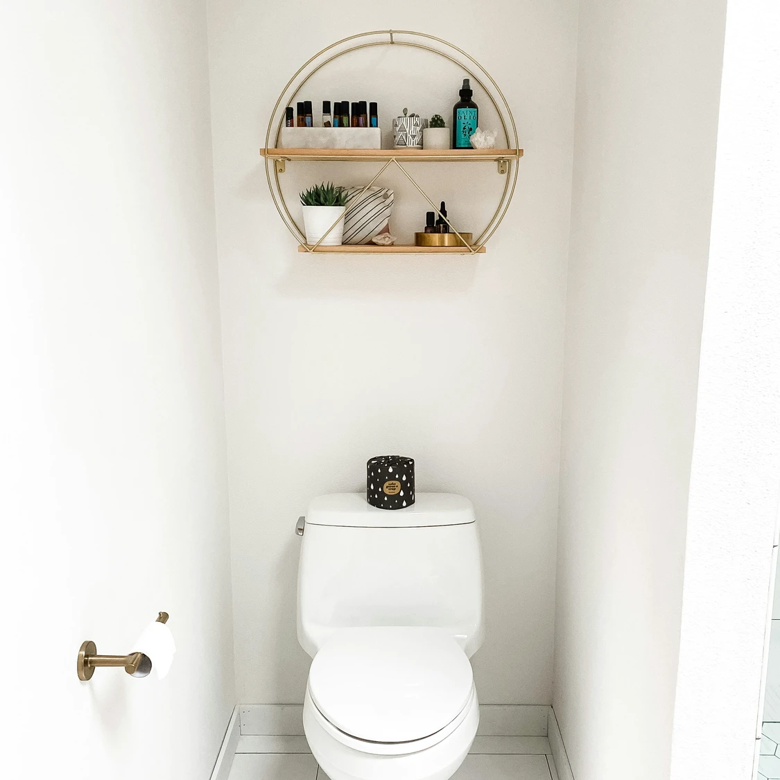 Modern white-tiled bathroom showcasing clever small bathroom ideas on a budget, featuring floating wooden shelves that make the most of the space above the toilet for stylish and functional storage.
