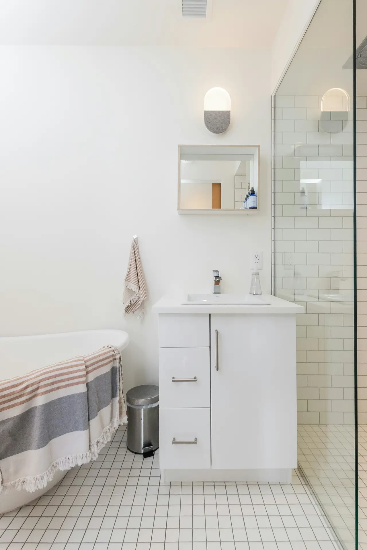 Bright small bathroom remodel with a mix of modern and classic touches, including a freestanding tub, glass shower, and compact vanity. The design choice to use light colors, white tiles, pale walls, and soft accents, creates an airy, spacious feel ideal for maximizing smaller spaces.