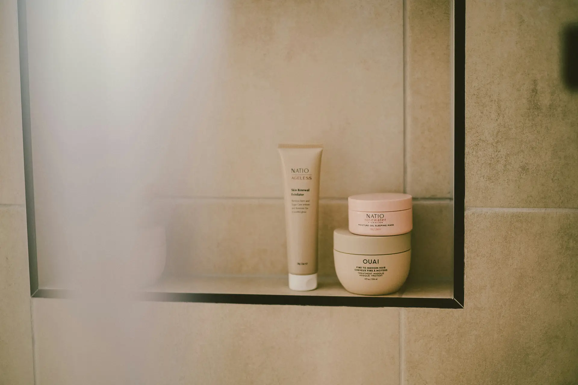 Built-in niche shelf in shower as part of a small bathroom remodel, showcasing neutral-toned tiles with neatly stored skincare products and hair treatments, offering both a stylish and functional storage solution.