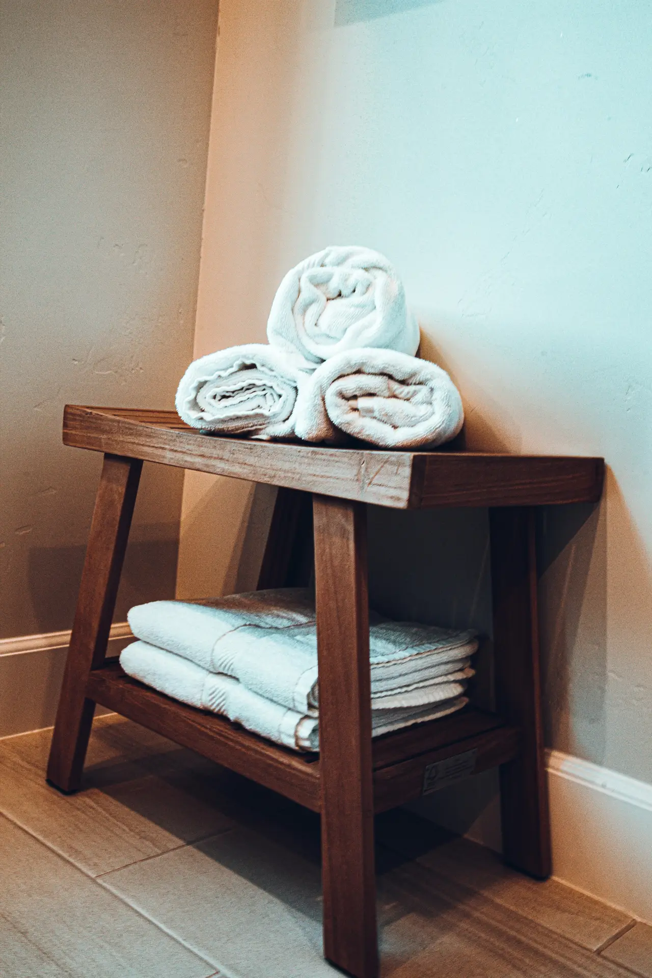 Wooden bench used for towel storage in a small bathroom remodel, featuring neatly folded and rolled single color textiles in crisp white, adding a clean and spa-like touch to the space.