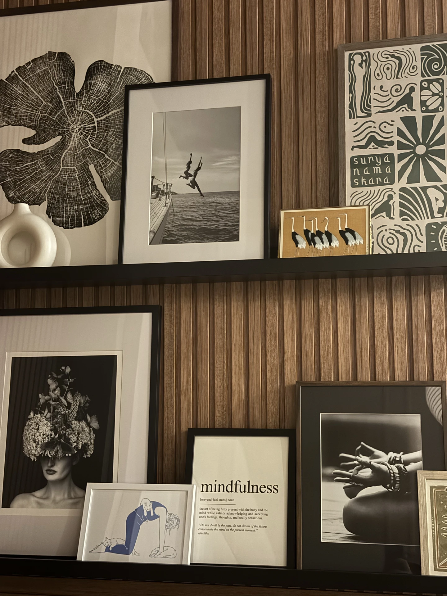 A creative approach to small bedroom decor, featuring a dark wooden accent wall with a sleek picture rail instead of big pictures. Various framed artworks and photographs in black, white, and muted tones lean casually on the ledge, creating a layered gallery look without overwhelming the space. The mix of abstract art, photography, and typography adds personality and balance, while keeping the room stylish and uncluttered.