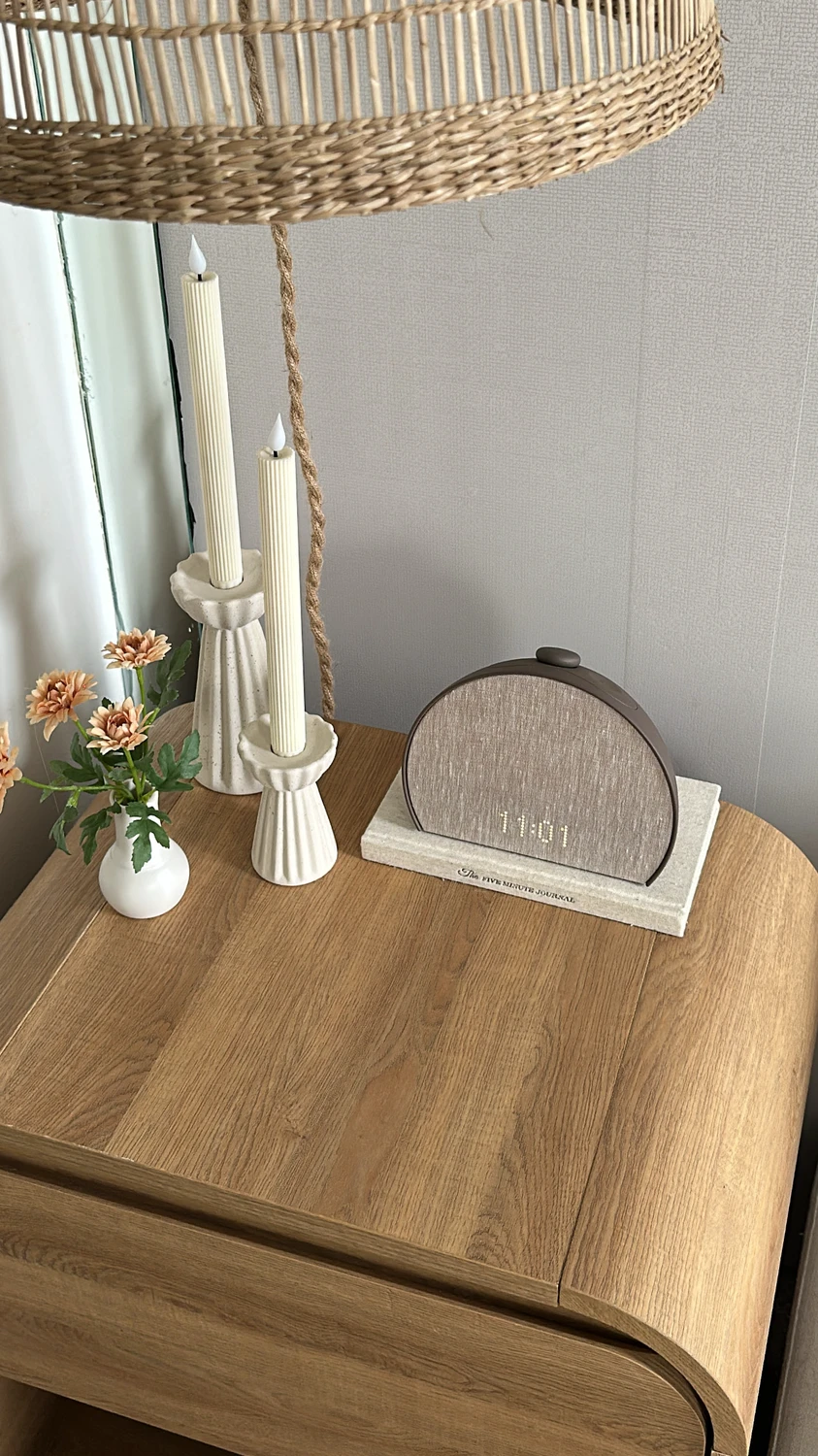 Minimalist setup with a wooden floating nightstand, decorated with ribbed candlesticks, a digital clock, and a small vase of flowers, showcasing clever small bedroom ideas with storage. The clean lines and light textures create a cozy yet functional space-saving solution.