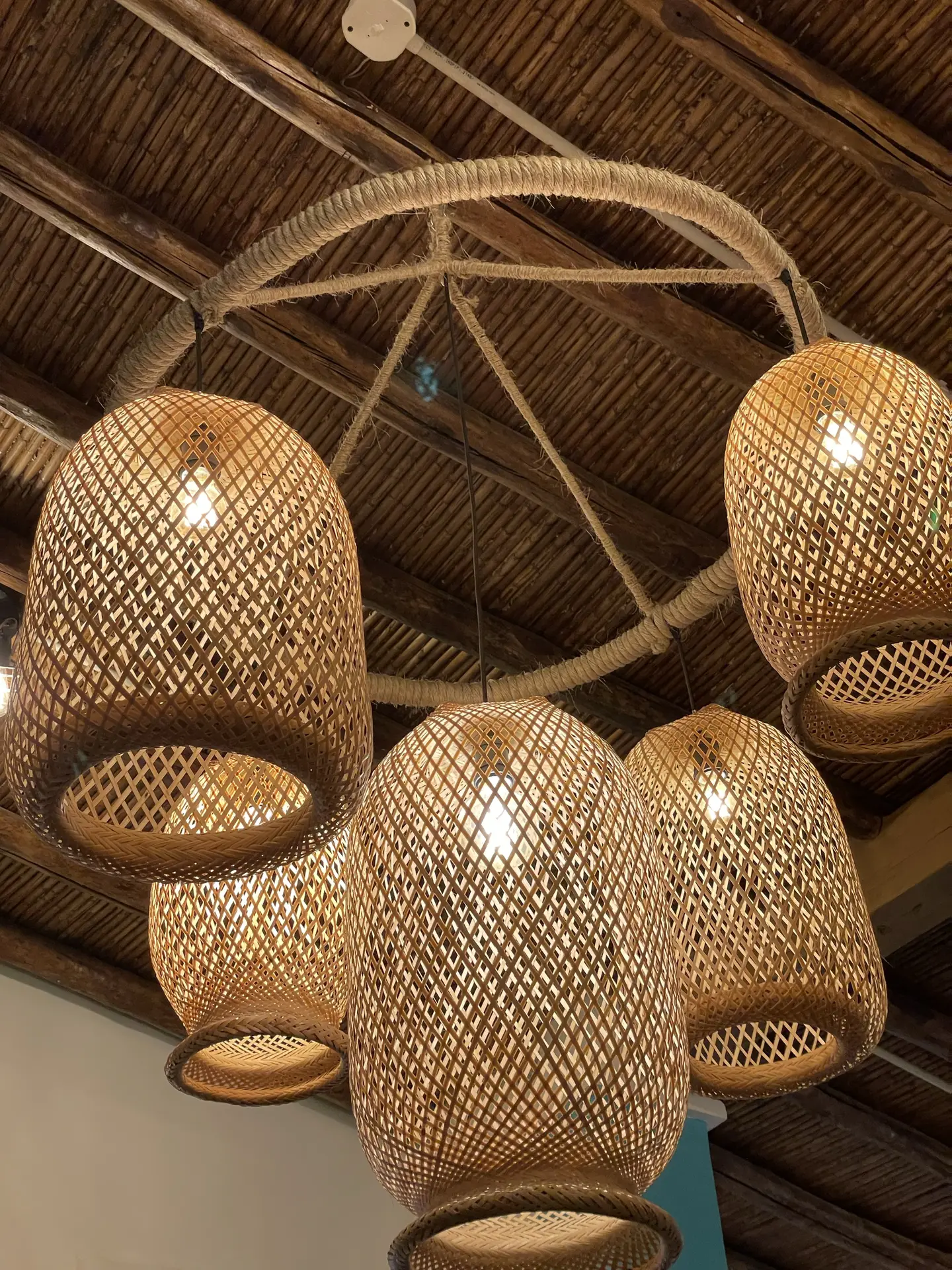 A cluster of boho rattan pendant lights hangs from a rustic wooden ceiling, creating a warm and inviting glow. The natural materials and woven texture add charm and character, serving as beautiful inspiration for outdoor lighting ideas that bring a cozy, handcrafted touch to patios or covered terraces.