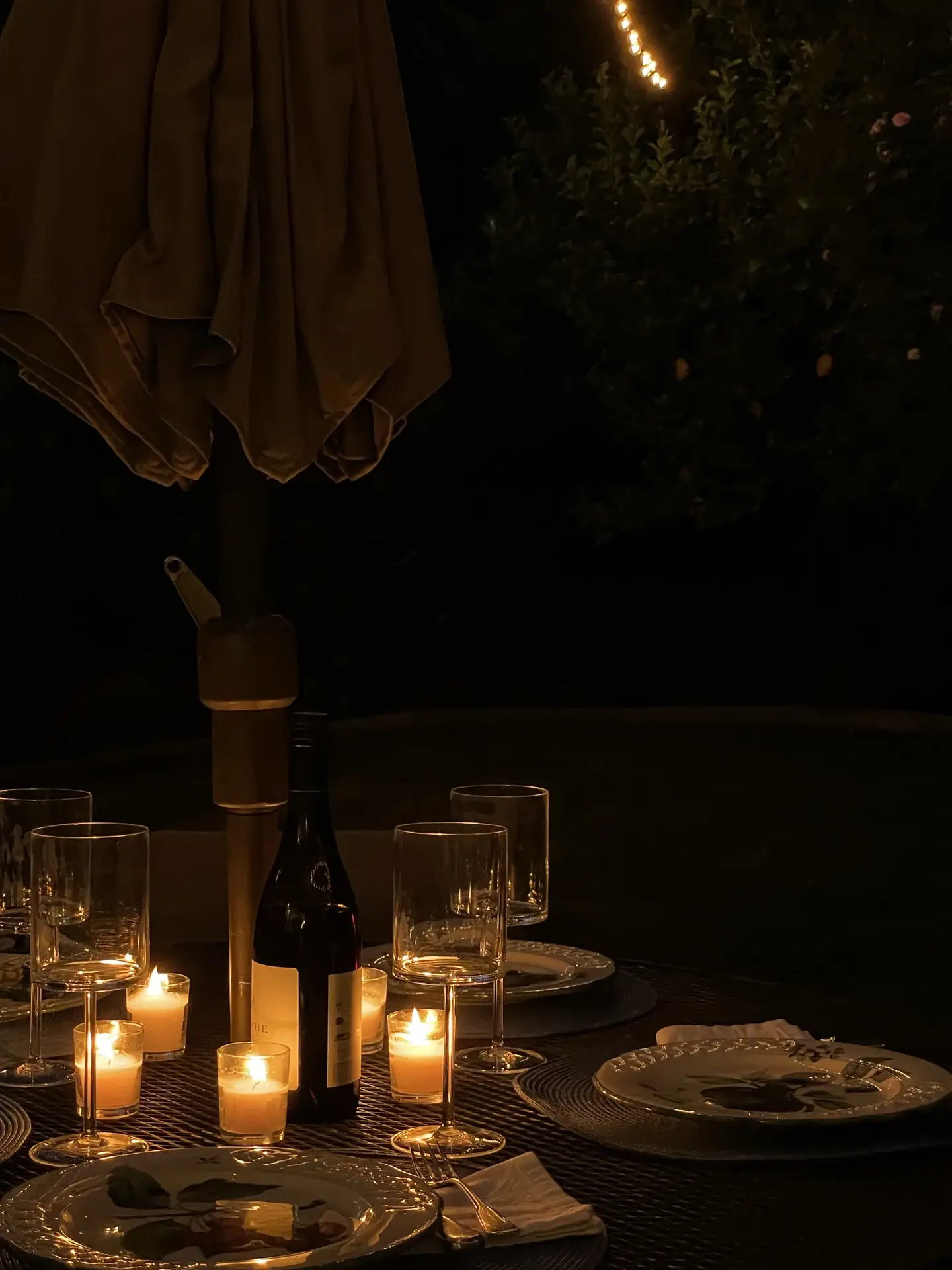 A cozy evening dinner setup outdoors, with a table beautifully arranged with plates, wine glasses, and softly glowing candles creating a romantic ambiance. The warm flicker of candlelight adds charm and intimacy to the scene, offering timeless outdoor lighting ideas for relaxed gatherings or intimate meals under the night sky.