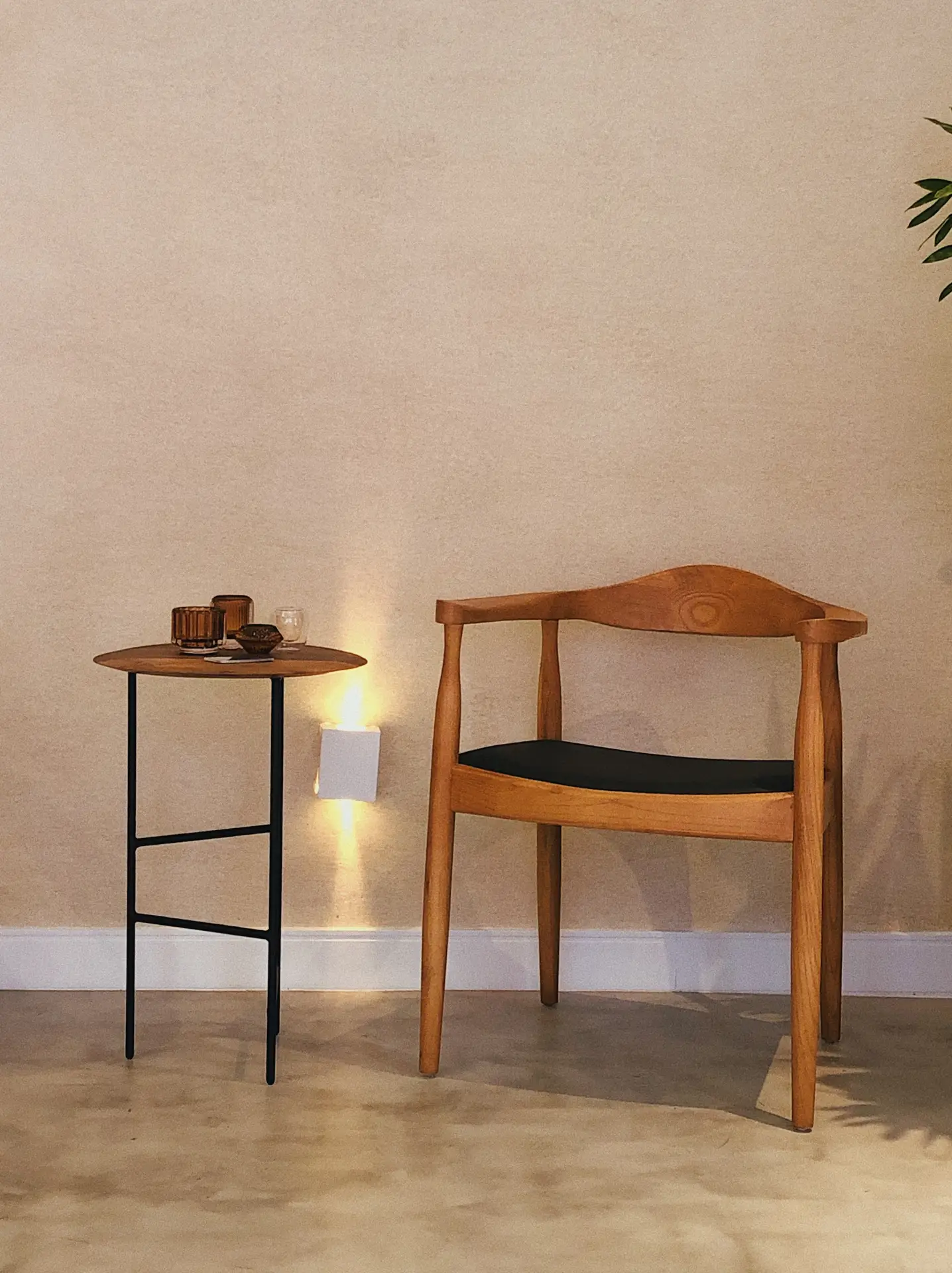 A minimalist seating area featuring a wooden chair, a small round side table, and a soft wall washer light illuminating the textured wall behind. The warm, indirect glow adds depth and coziness, making it a stylish example of outdoor lighting ideas suitable for patios, entryways, or covered terraces.