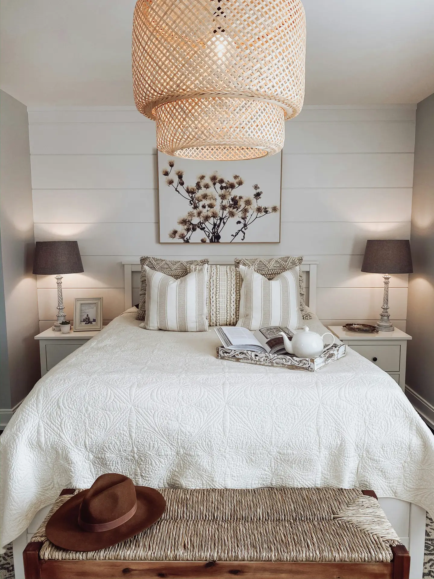 A cozy bedroom styled with layered neutral bedding, matching nightstands, and warm lighting, featuring a woven bench or ottoman at the foot of the bed for extra texture and practicality. Soft patterns, natural materials, and calm tones make this a great example of bedroom ideas that blend comfort with timeless charm.