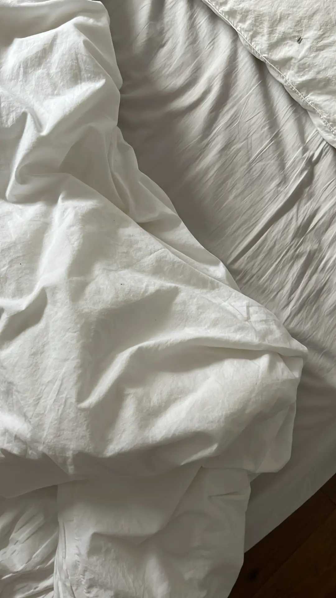 A close-up of softly wrinkled white linen bedding draped across a mattress, offering bedroom ideas that highlight the relaxed, natural texture of linen bedding. Gentle light falls across the fabric, creating a calm and lived-in atmosphere perfect for a cozy, effortless bedroom style.