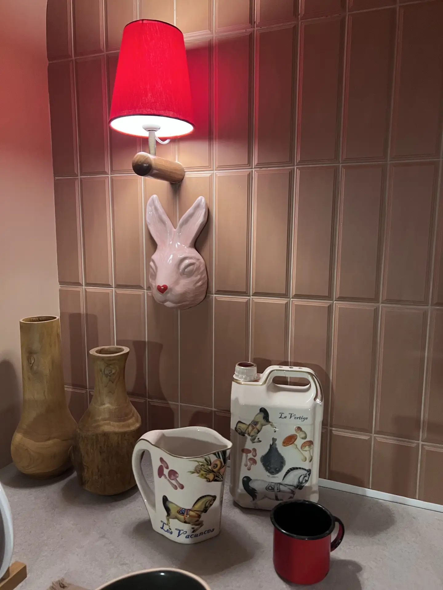 A cozy corner of a kitchen featuring a warm-toned backsplash with fluted tiles, paired with a red wall lamp and decorative ceramics. The vertical ridges of the tiles add depth and texture to the design, offering creative kitchen backsplash ideas that bring a touch of character and vintage charm to any space.