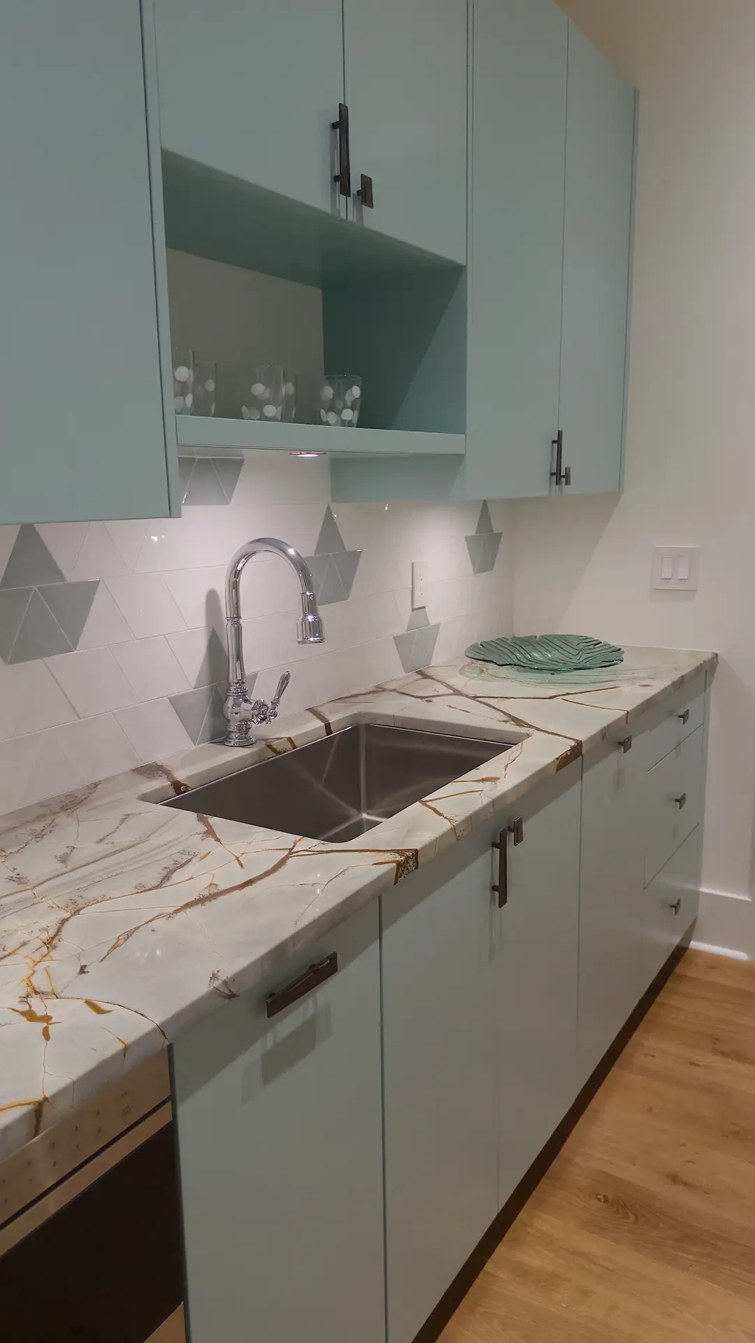 A contemporary kitchen with mint green cabinets, a marble-look countertop, and a backsplash featuring geometric hexagon tiles in soft gray and white. The pattern adds visual interest without overpowering the space, serving as modern kitchen backsplash ideas for a clean yet playful design aesthetic.