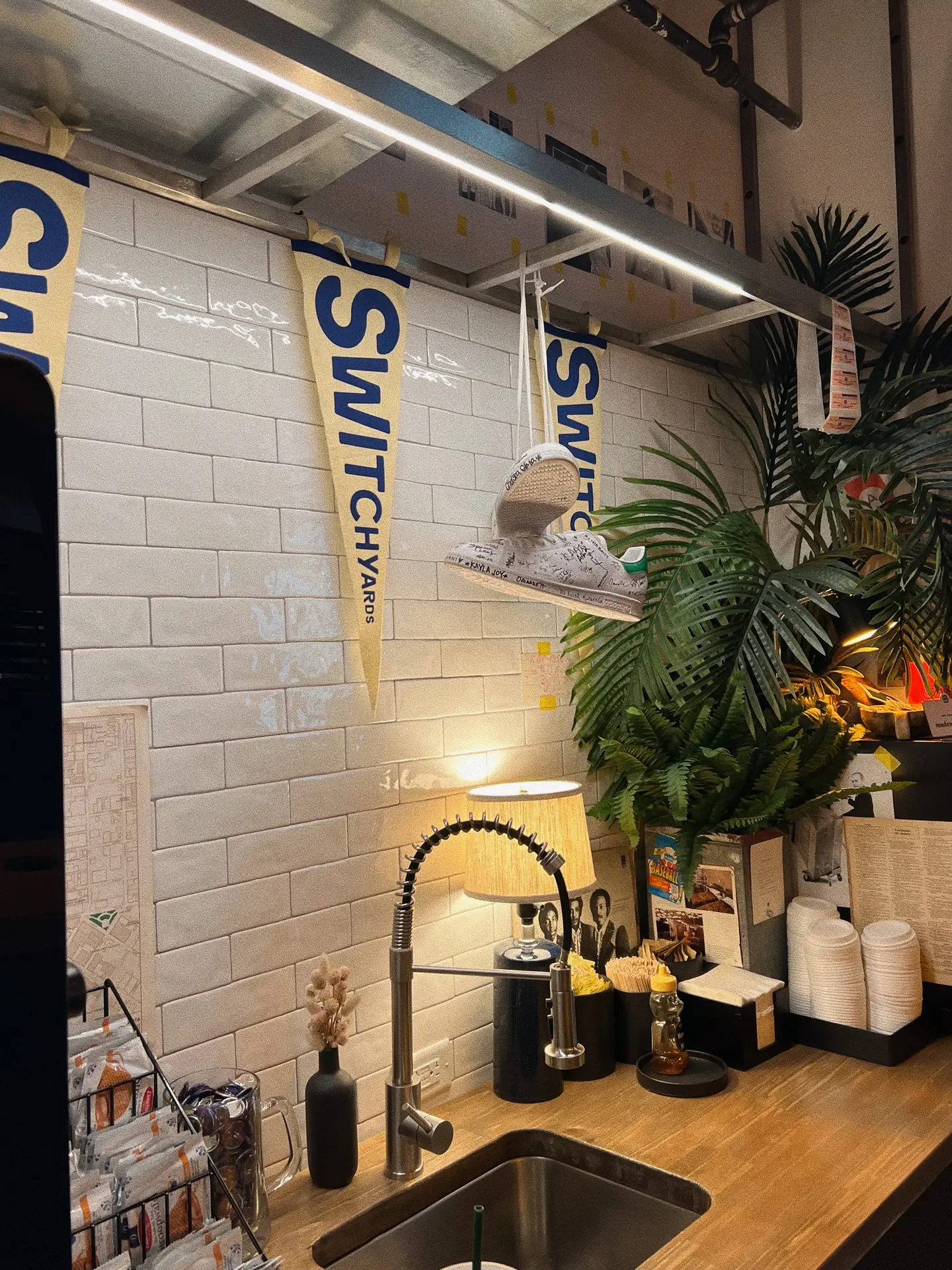 A cozy and eclectic coffee corner featuring a wooden countertop, industrial faucet, and white handmade-look subway tiles as the backsplash. The space is decorated with pennants, plants, and warm lighting, creating a relaxed and creative vibe. A great example of kitchen backsplash ideas that mix modern finishes with personal touches.