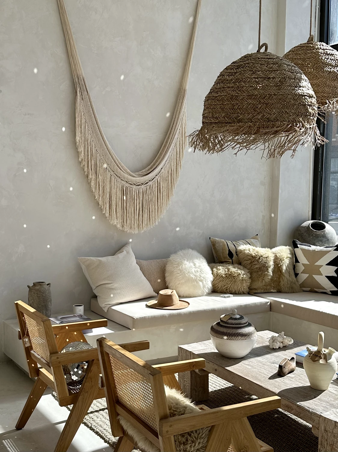 A sunlit boho living room featuring woven pendant lights, natural wood furniture, and neutral-toned cushions with layered textures. The wall decor and earthy materials add a relaxed, organic feel, offering living room ideas that emphasize warmth, craftsmanship, and effortless style.