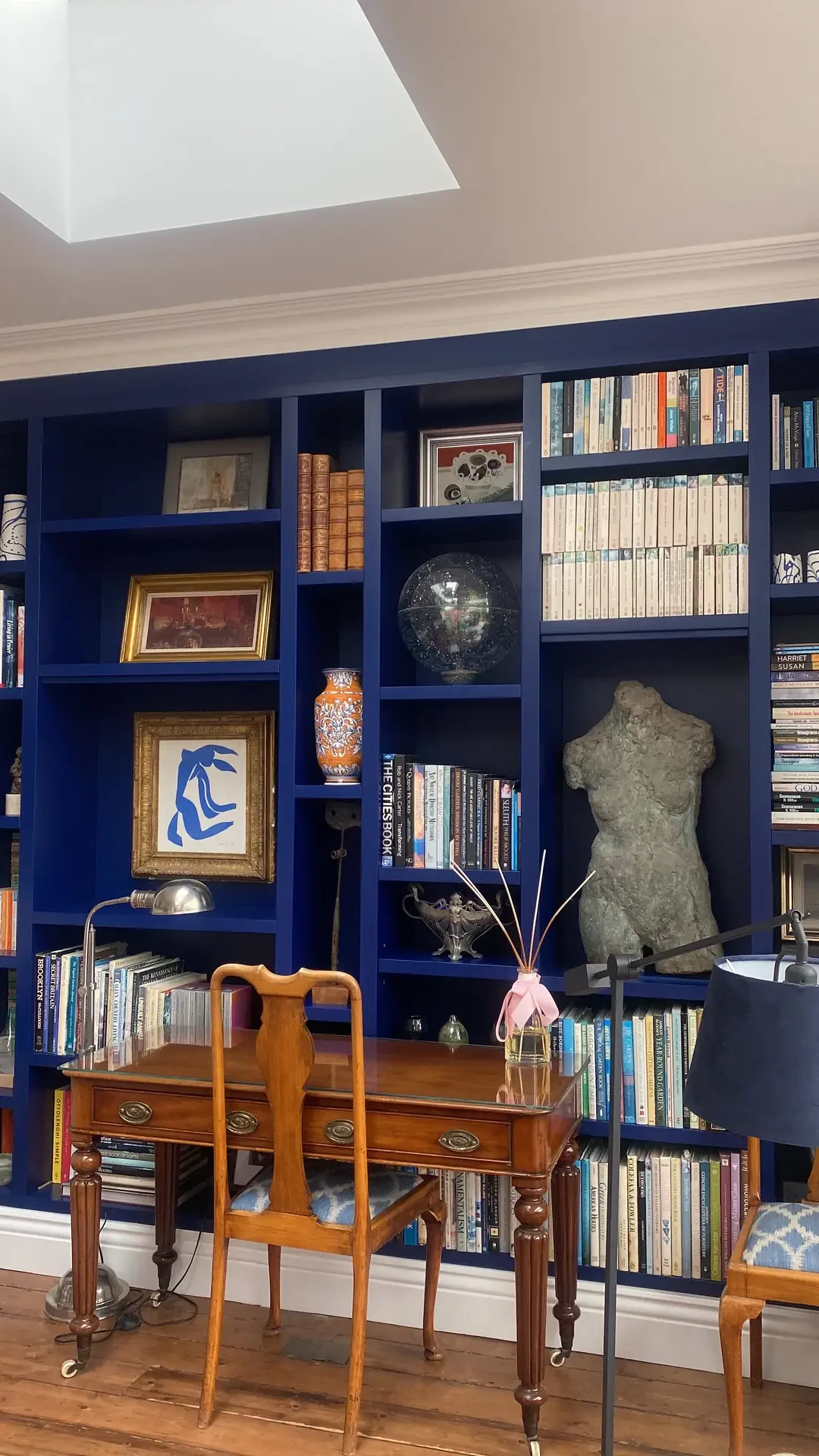 A stylish living room corner with a striking deep blue built-in storage unit filled with books, framed art, and decorative objects. A vintage wooden desk with matching chairs adds warmth and contrast, showcasing living room ideas that blend functional built-in storage with curated personal touches for a sophisticated yet inviting space.
