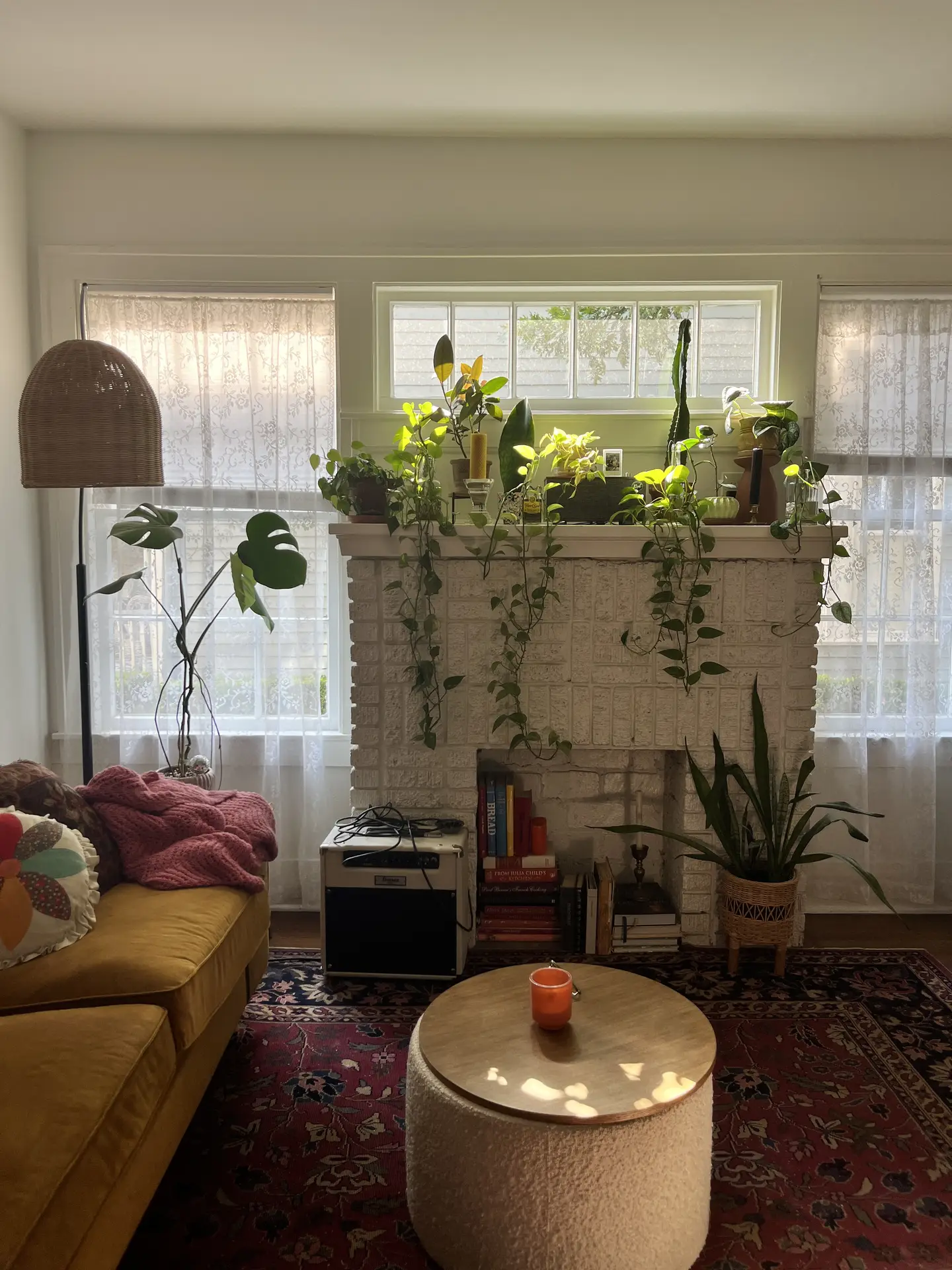 A cozy living room filled with natural light, showcasing a white painted brick fireplace adorned with lush plants cascading down the mantel. A mustard yellow sofa, boho rug, and wooden coffee table complete the look, offering living room ideas centered on greenery integration for a warm and inviting atmosphere.