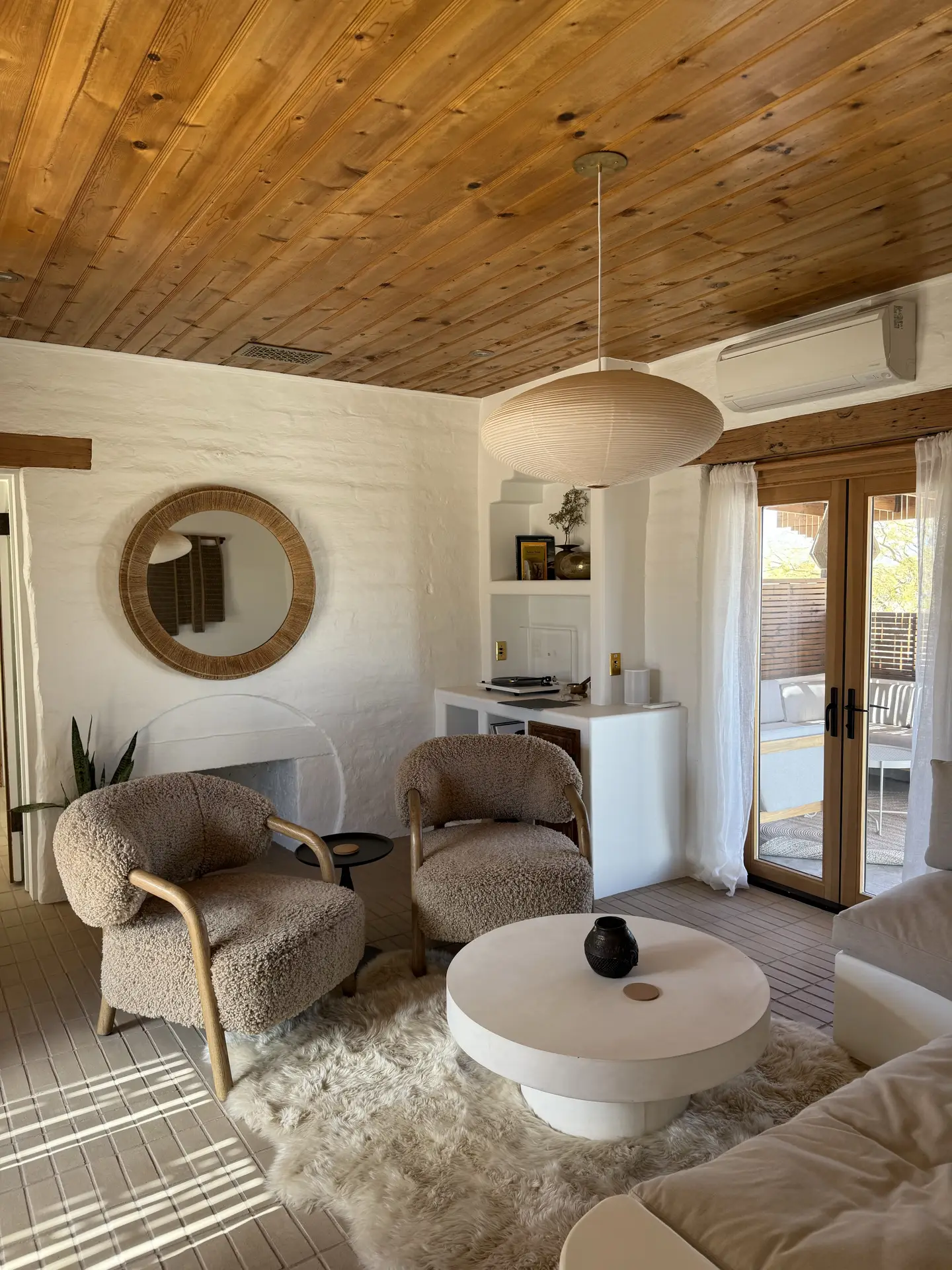 A warm and inviting living room featuring a mix and match seating arrangement with textured armchairs, a soft sofa, and a round coffee table on a fluffy rug. The wooden ceiling and neutral color palette add natural charm, offering living room ideas that balance coziness with modern design.