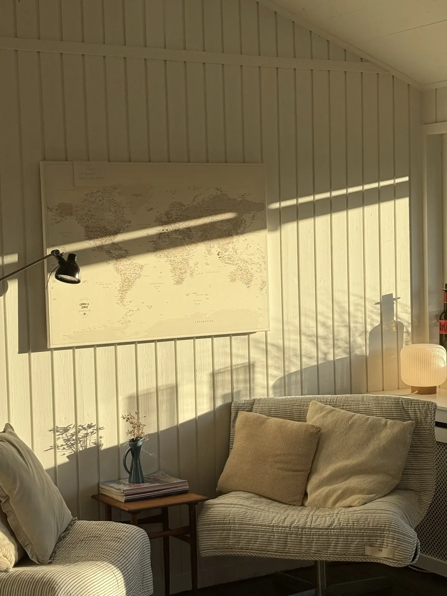 A serene living room nook bathed in golden sunlight, featuring two striped armchairs with soft beige cushions, a small wooden side table, and a minimalist wall map. The warm tones and simple decor capture living room ideas inspired by a Scandinavian hygge-corner, emphasizing comfort, light, and understated elegance.