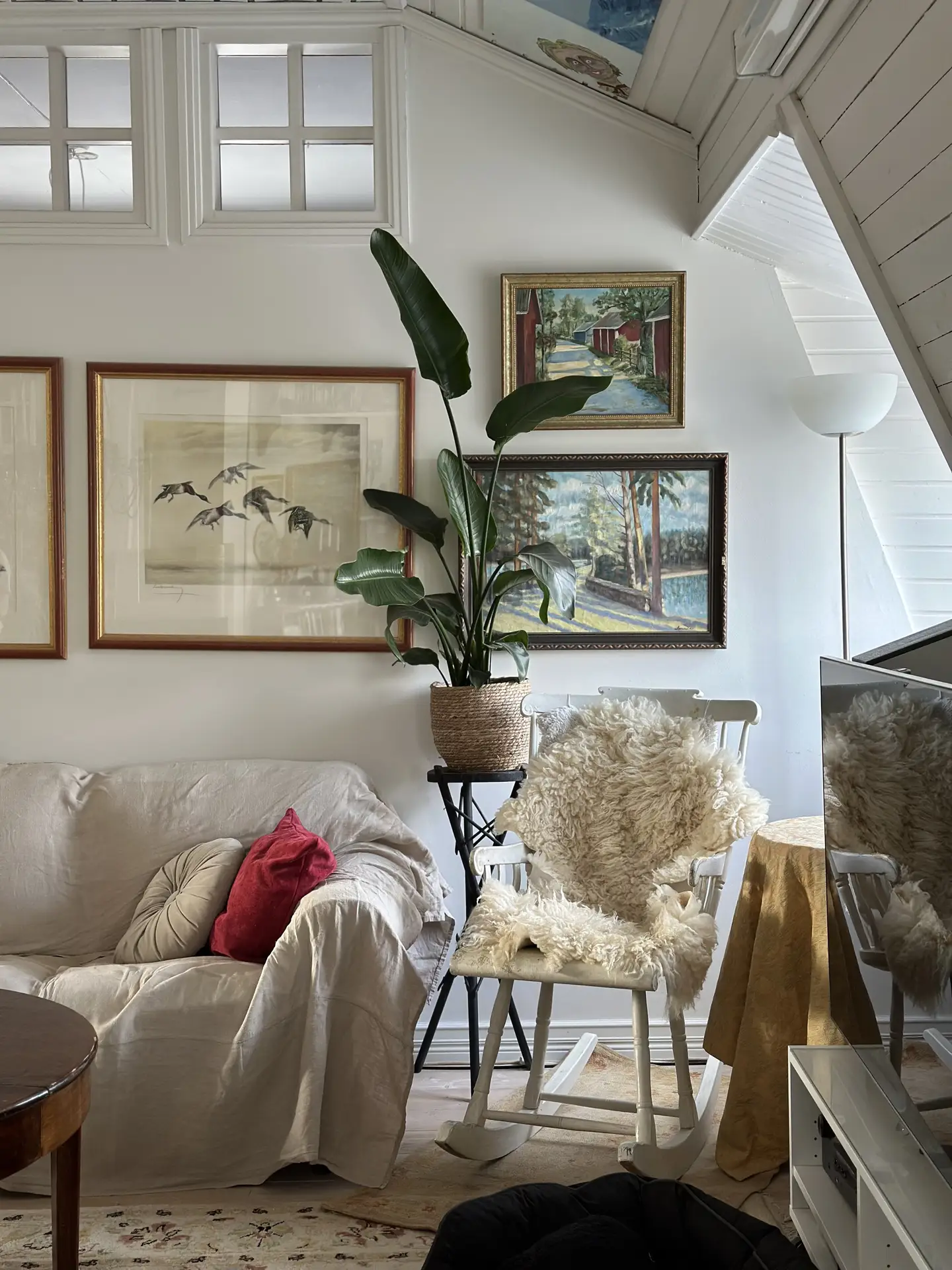 A charming living room filled with soft textures and natural light, featuring a neutral sofa with layered pillows, a rocking chair draped in a fluffy throw, and framed artwork on the wall. This setup highlights living room ideas focused on textile layering to create a warm and inviting atmosphere.
