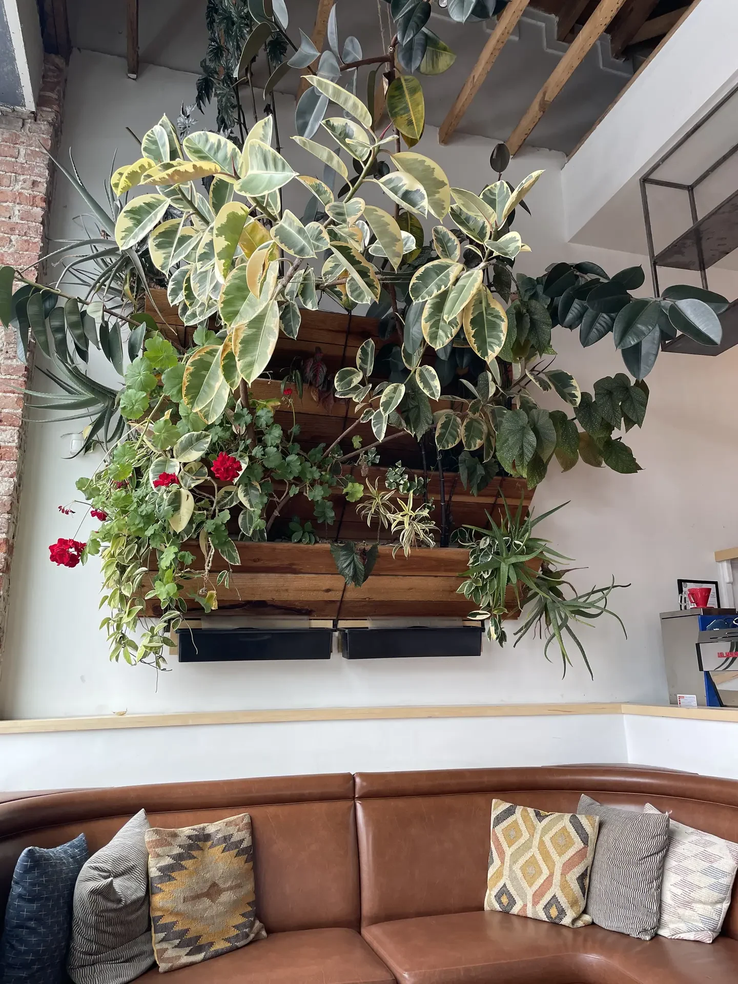 A contemporary living room featuring a brown leather sofa with patterned cushions and a lush vertical garden made of wooden panels filled with vibrant green plants. The mix of natural textures and greenery adds warmth and freshness, offering living room ideas that use a vertical garden to bring life and depth into modern interiors.