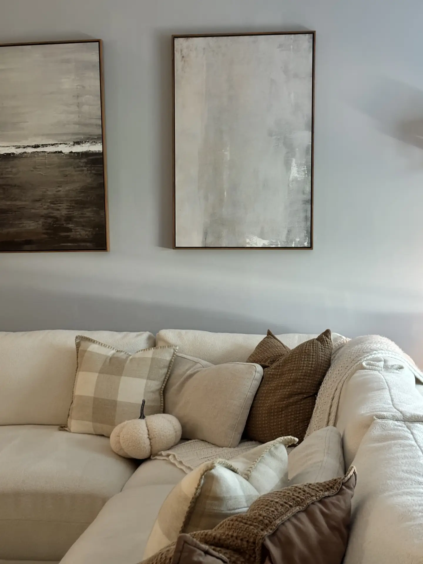 A cozy corner sofa filled with neutral throw pillows, knits, and a small fabric pumpkin shows how small living room decor can benefit from thoughtful texture layering. Soft blankets, woven cushions, and muted artwork on the wall create a warm, inviting atmosphere that feels balanced and adaptable to many interior styles.