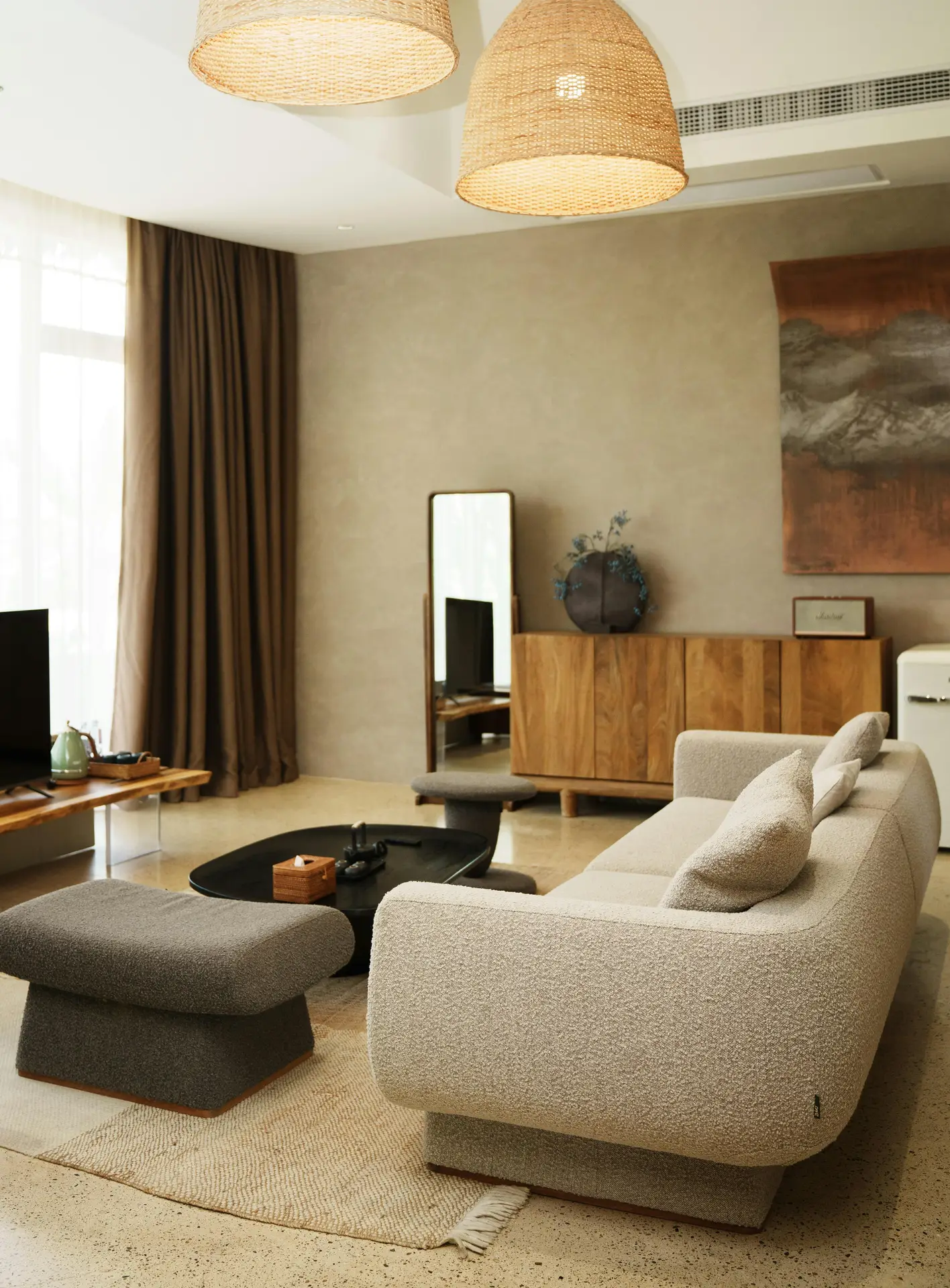 A warm and inviting space styled with small living room decor, featuring a curved textured sofa, matching ottoman, and a black coffee table set on layered neutral rugs. Natural wood accents, soft brown curtains, and a standing mirror blend seamlessly into a tone-in-tone palette, creating a calm and cohesive look that suits various interior styles.