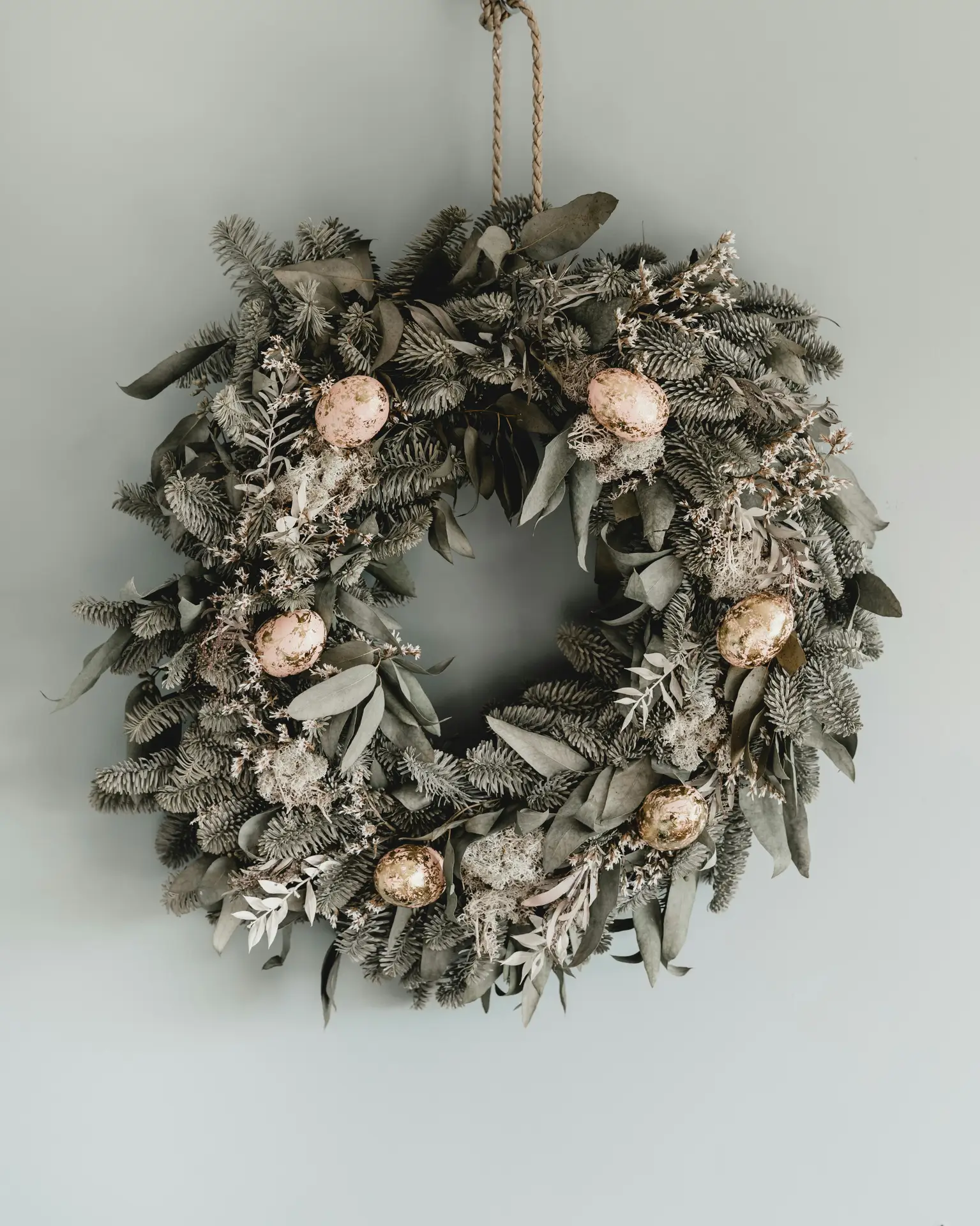 Easter decor ideas showcasing an easter wreath variation made from muted greenery and soft eucalyptus tones, accented with delicate dried foliage and small decorative eggs, hanging against a light wall for a natural, understated spring look.