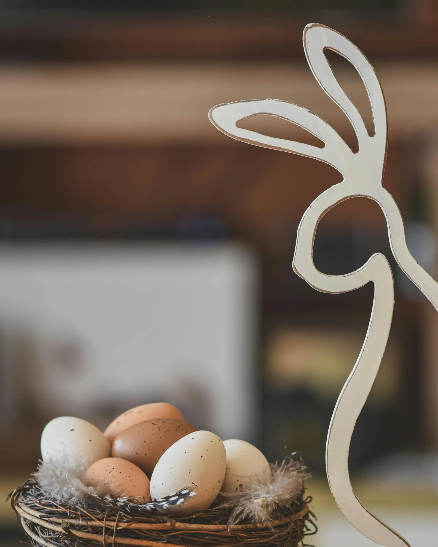 Easter decor ideas featuring a minimalist bunny figure with egg nest, showing a simple wooden bunny silhouette next to a small woven nest filled with neutral speckled eggs and soft feathers, styled against a softly blurred indoor background.