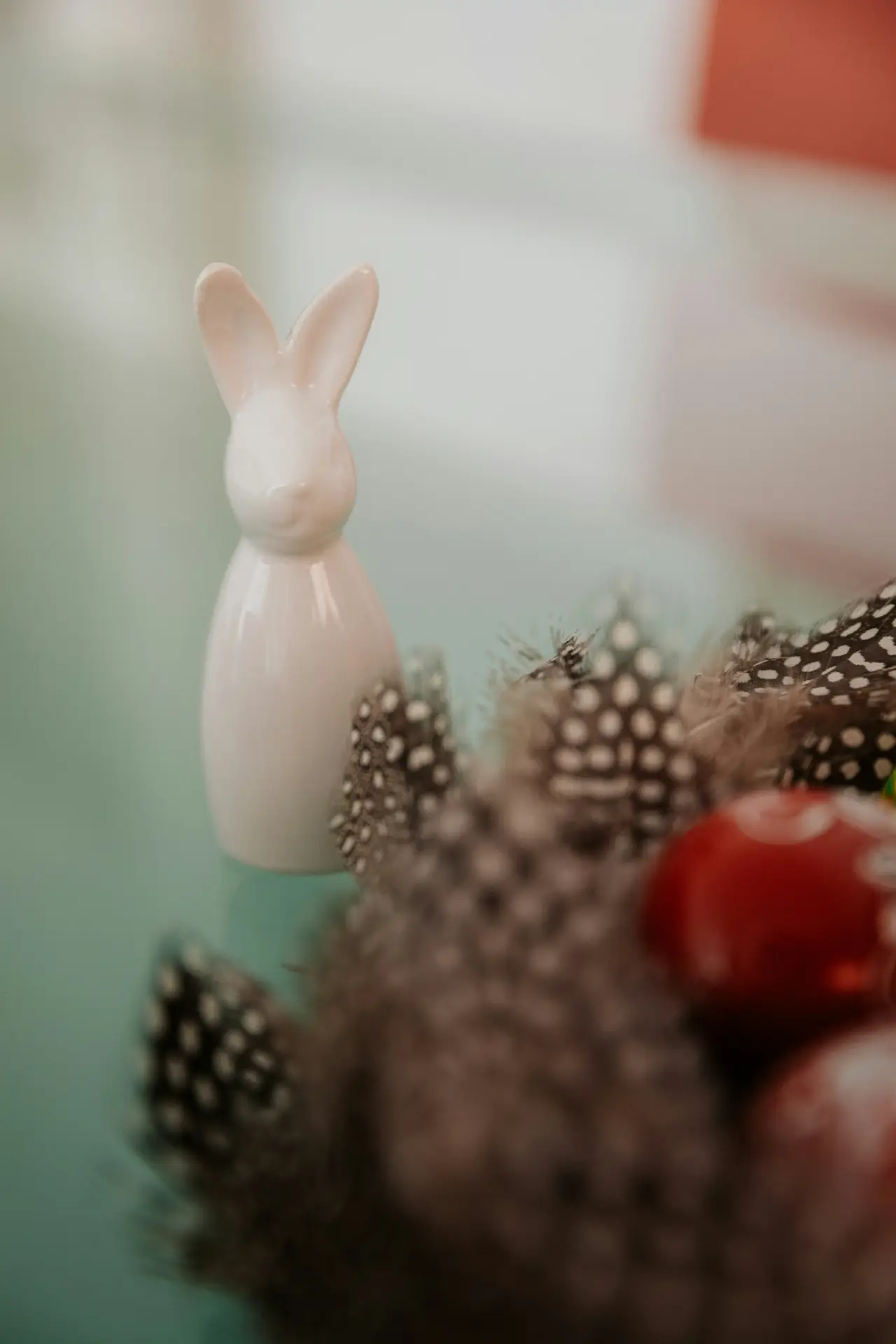 Easter decor ideas featuring a delicate porcelain bunny figure placed beside a decorative nest with feathers and colorful eggs, creating a soft seasonal accent suitable for shelves, tables, or springtime displays.
