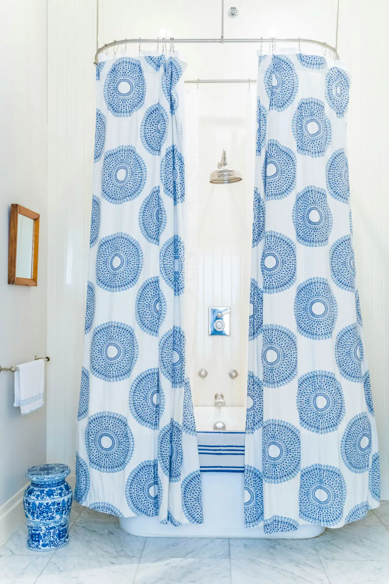 A bright, classic bathroom with a freestanding tub framed by a patterned shower curtain in white and blue, featuring repeating circular motifs. The scene fits girls bathroom ideas by showing how a patterned shower curtain can add visual interest and color while keeping the space fresh, timeless, and easy to style.