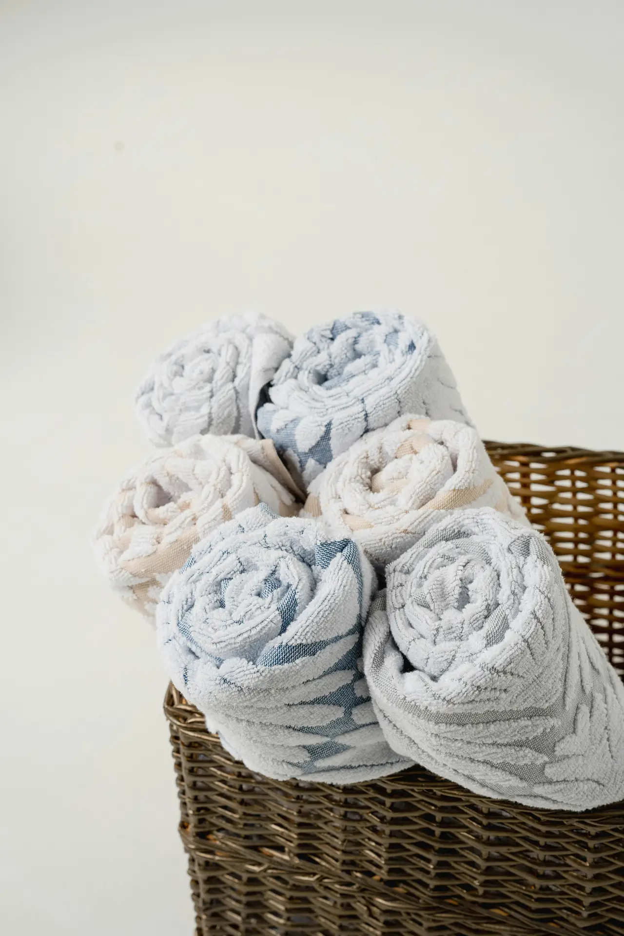 A woven basket filled with neatly rolled soft towels in light neutral and blue tones, set against a clean background. The mix of textures and gentle colors fits girls bathroom ideas by adding warmth, comfort, and an inviting spa-like feel through soft towels that work in both modern and cozy spaces.