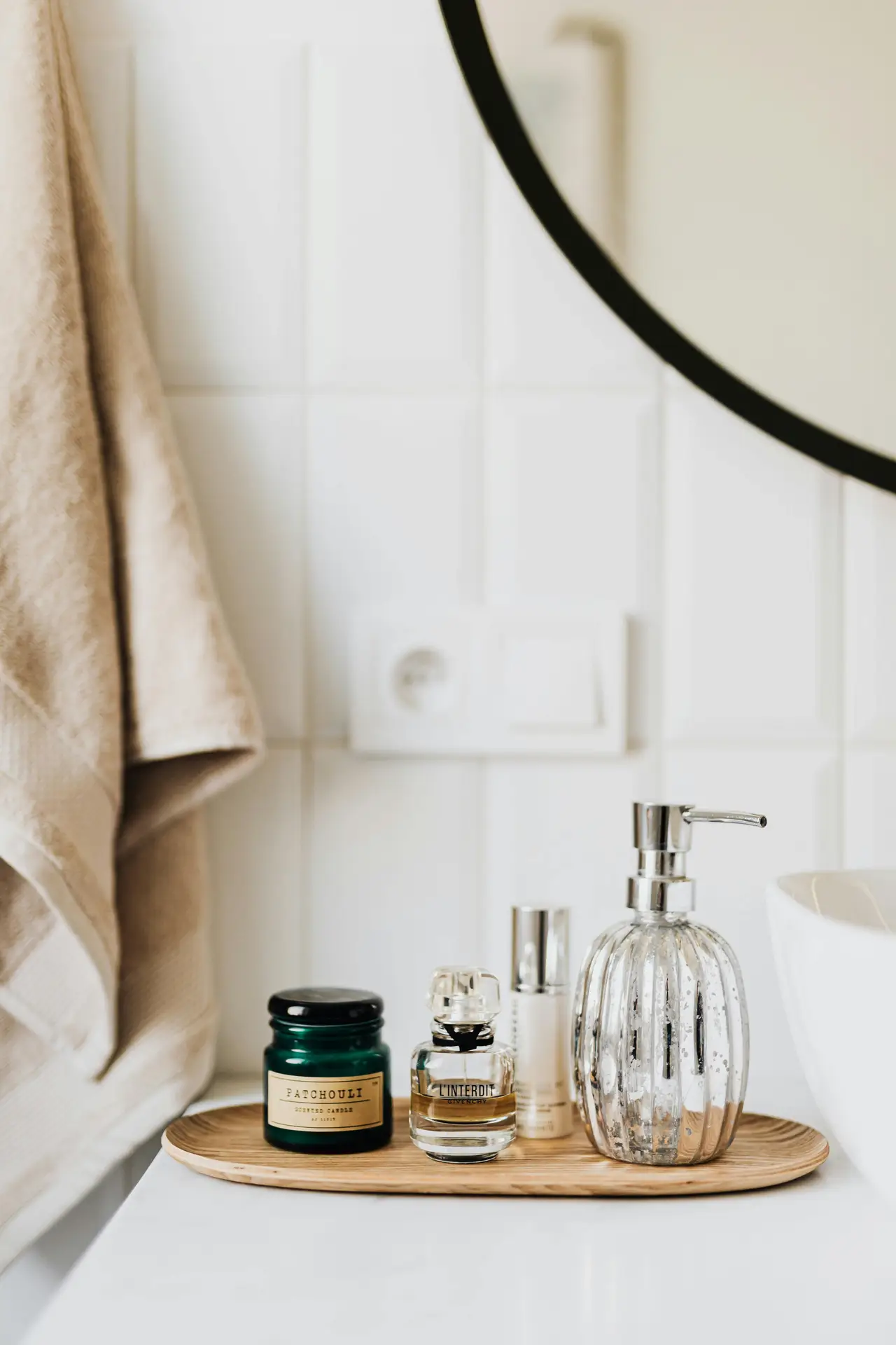 A styled bathroom vanity featuring a wooden tray that holds a soap dispenser, perfume bottles, and a small candle beside the sink. Neutral towels and clean white tiles create a soft, elegant look, offering girls bathroom ideas that use trays to keep everyday essentials organized while adding a decorative, spa-inspired touch.