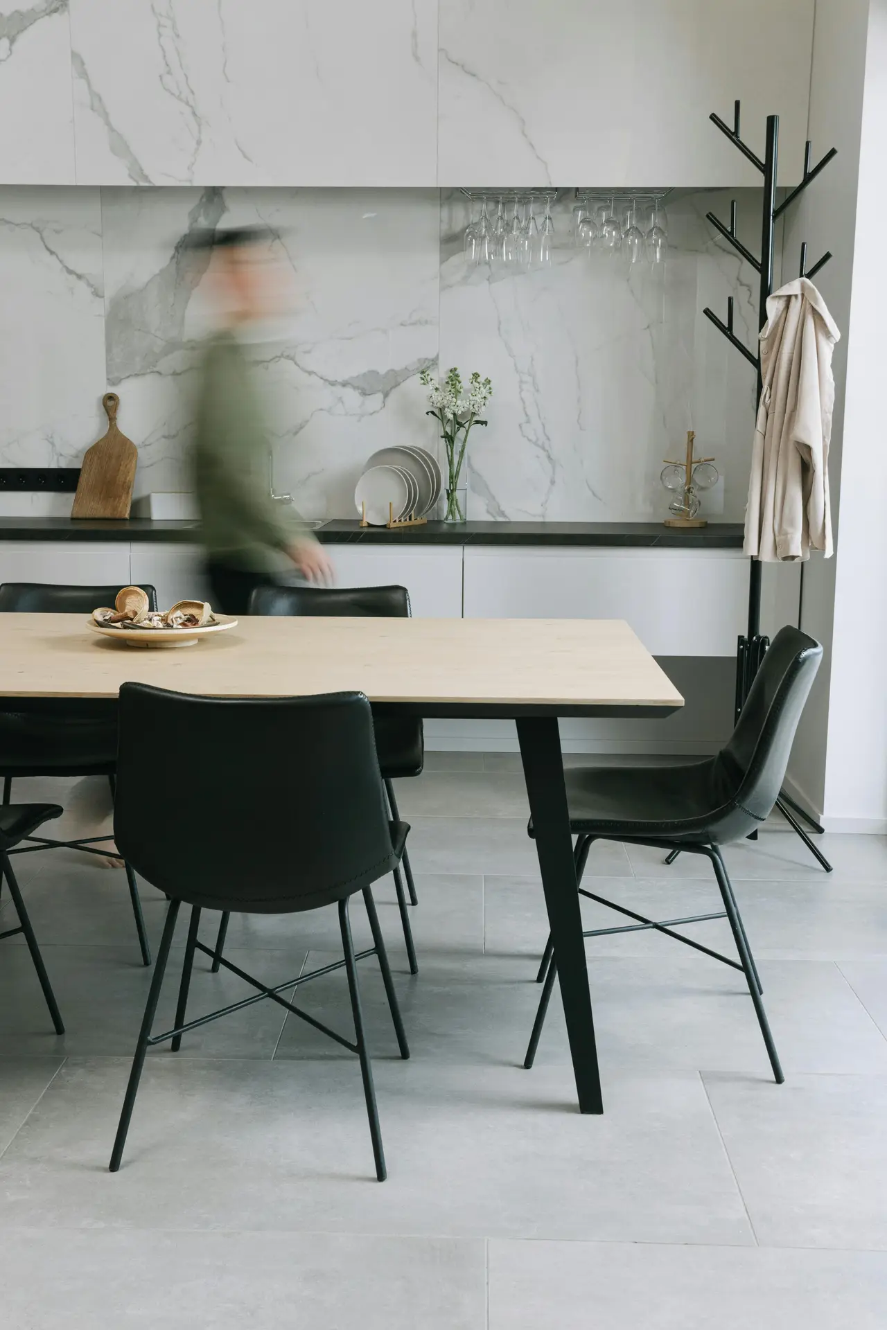 Sleek kitchen and dining space featuring marble-look walls, a light wood table, and black modern chairs, creating a neutral foundation, bold details through contrast; subtle décor and clean lines offer kitchen ideas for a minimalist yet striking interior.